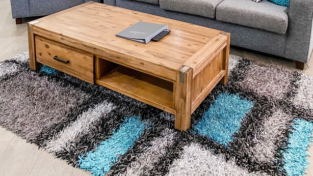 Una sala de estar moderna con un sofá gris, una mesa de centro de madera y un espejo grande en la pared.