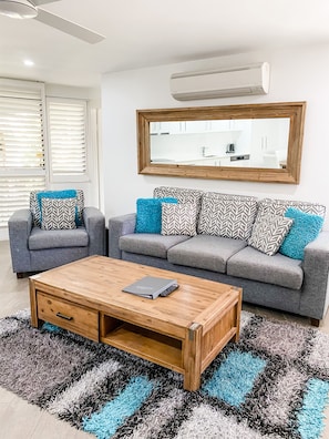 A modern living room with a grey sofa set, a wooden coffee table, and a large mirror on the wall. - Ocean Breeze Resort (Noosa Heads)