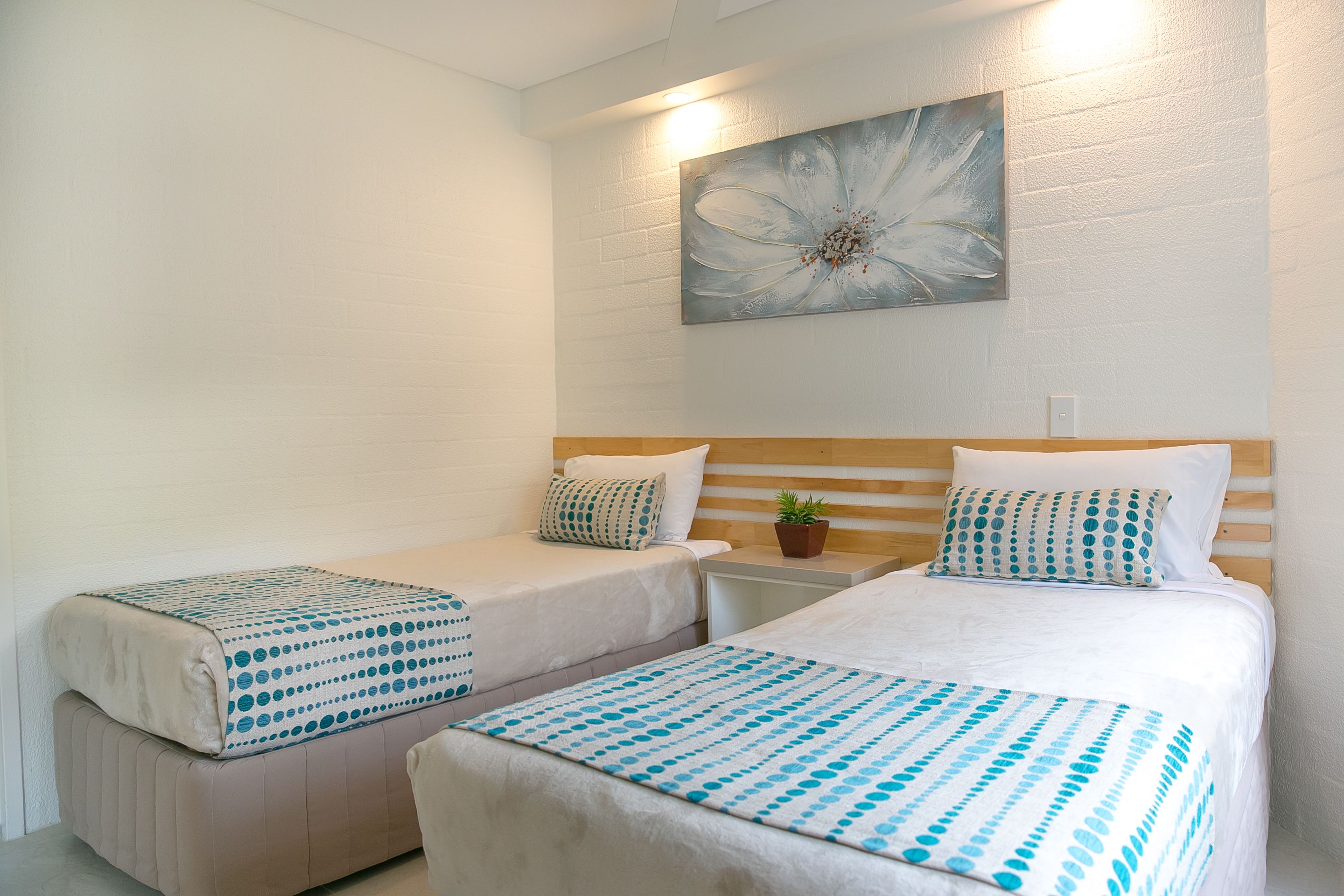 A hotel room with two beds, each with a blue and white polka dot bedspread, a wooden headboard, and a wall-mounted flower painting.