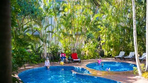 Un área de piscina con dos albercas, rodeada de palmeras y sillas de descanso.