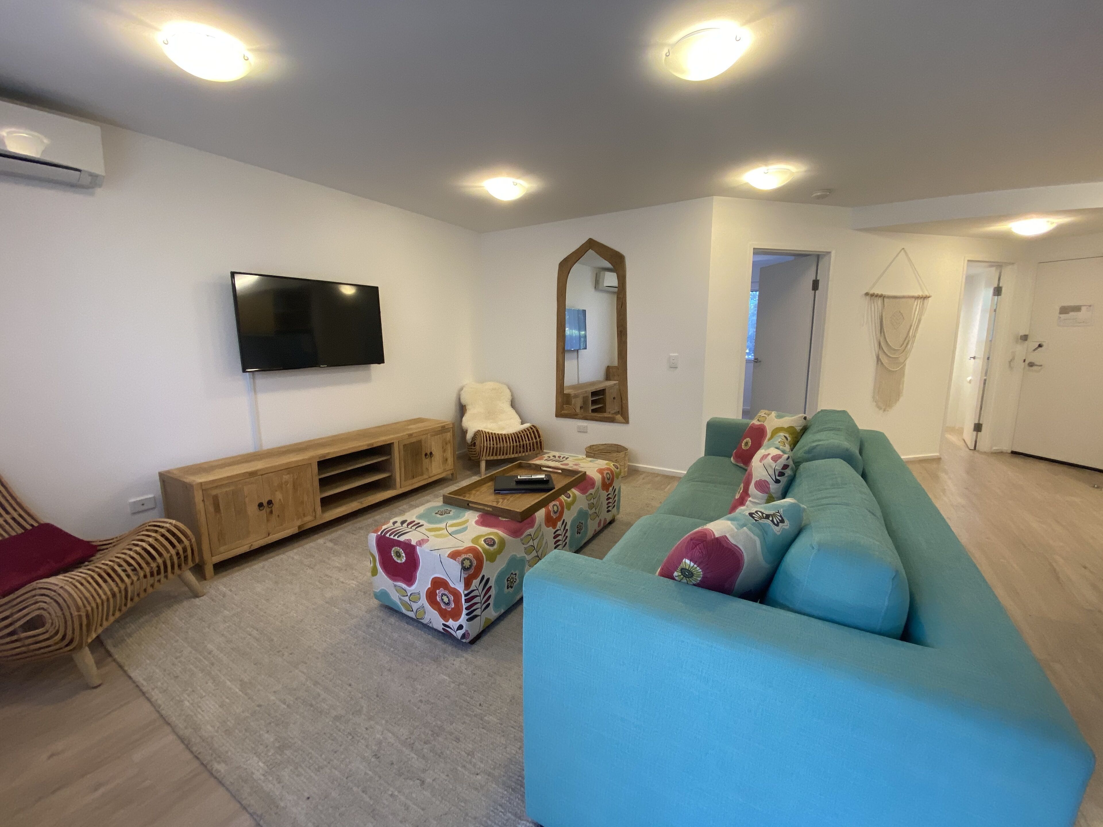 A modern living room with a teal sofa, a wooden entertainment unit, and a flat-screen TV mounted on the wall.