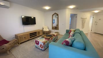 A modern living room with a teal sofa, a wooden entertainment unit, and a flat-screen TV mounted on the wall.