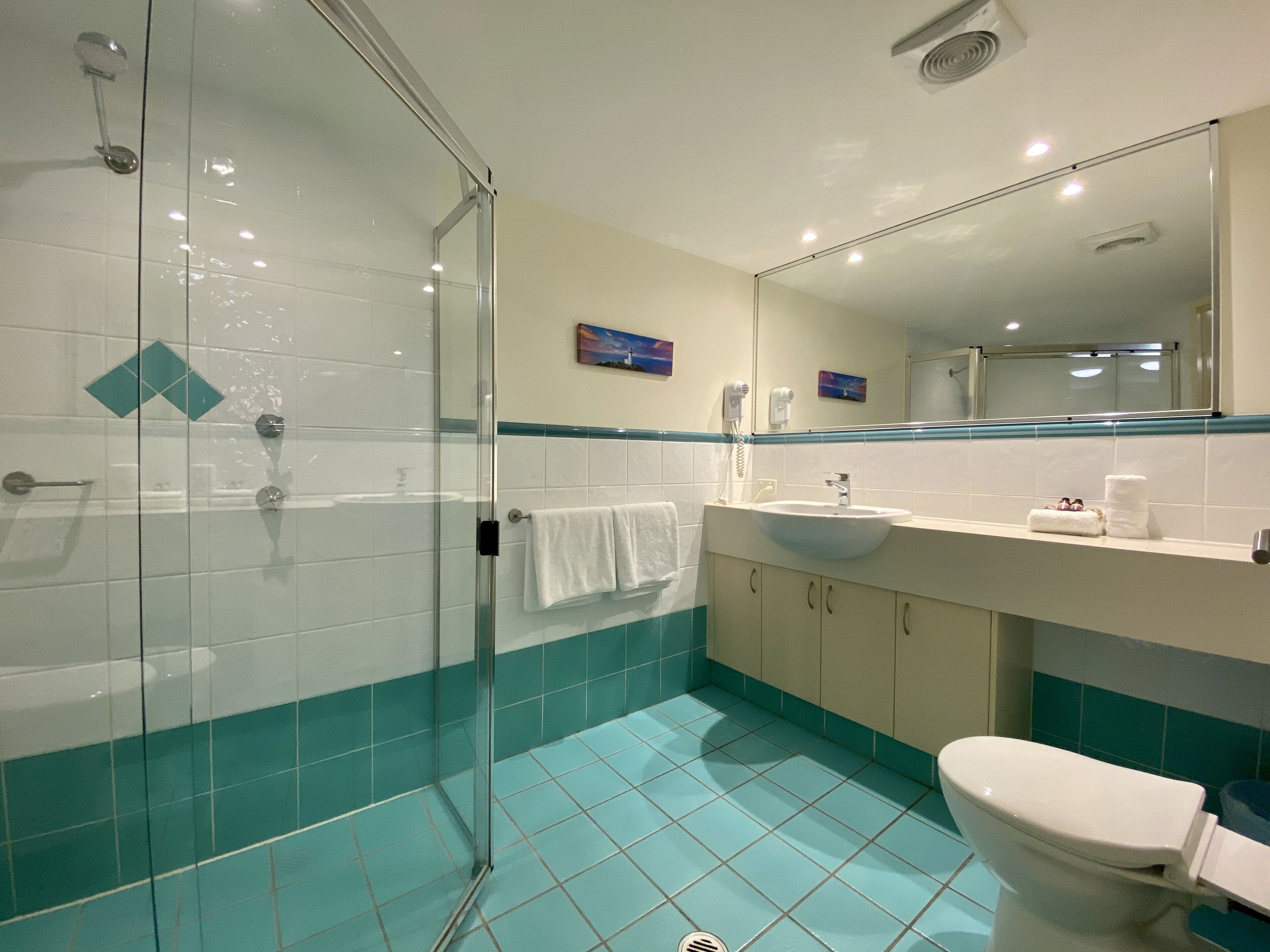 Une salle de bain avec une douche à parois de verre, un lavabo, des toilettes et des carreaux de couleur turquoise.