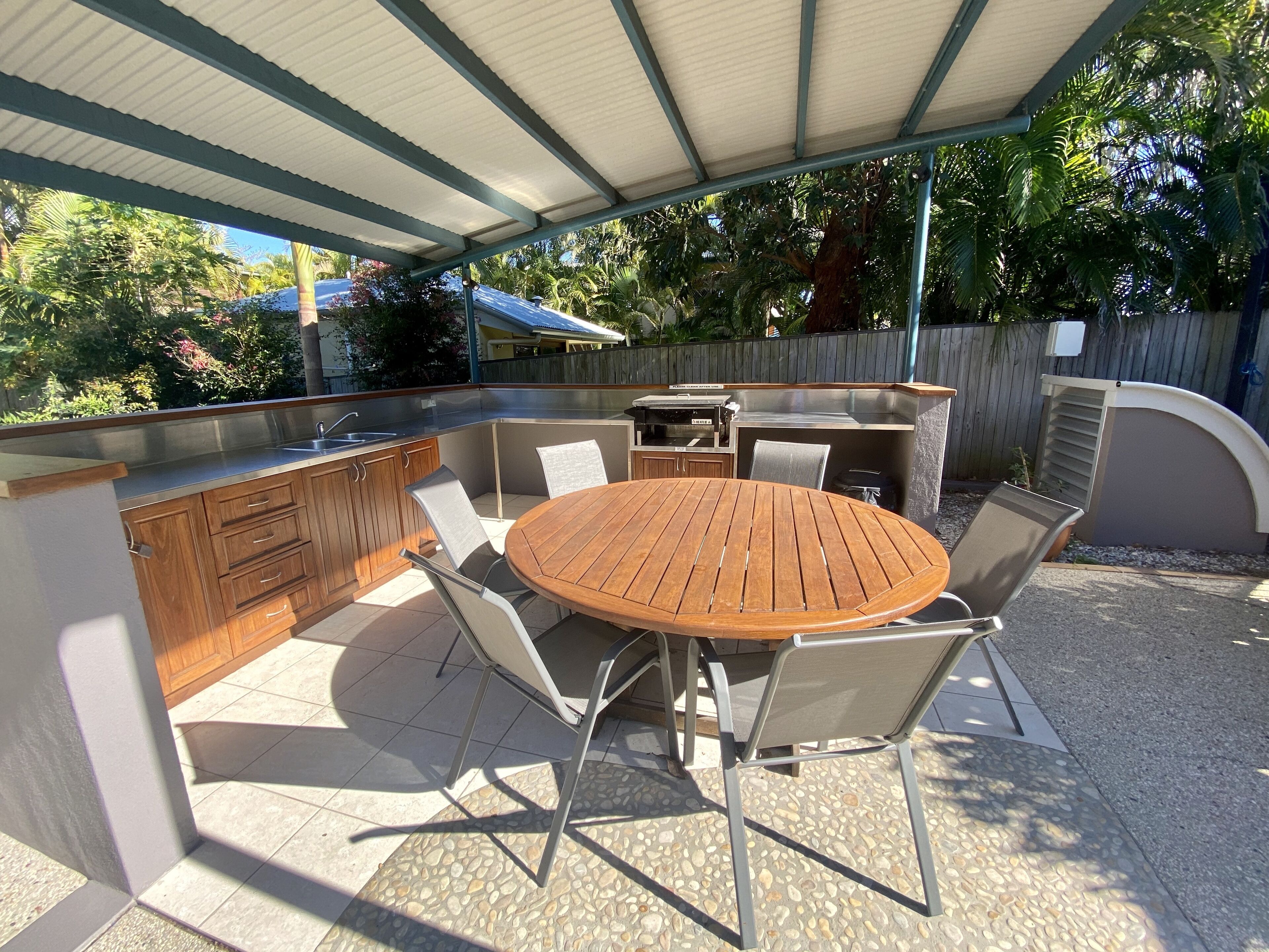 Una cocina exterior con una mesa redonda y sillas, un lavamanos integrado y una parrilla.