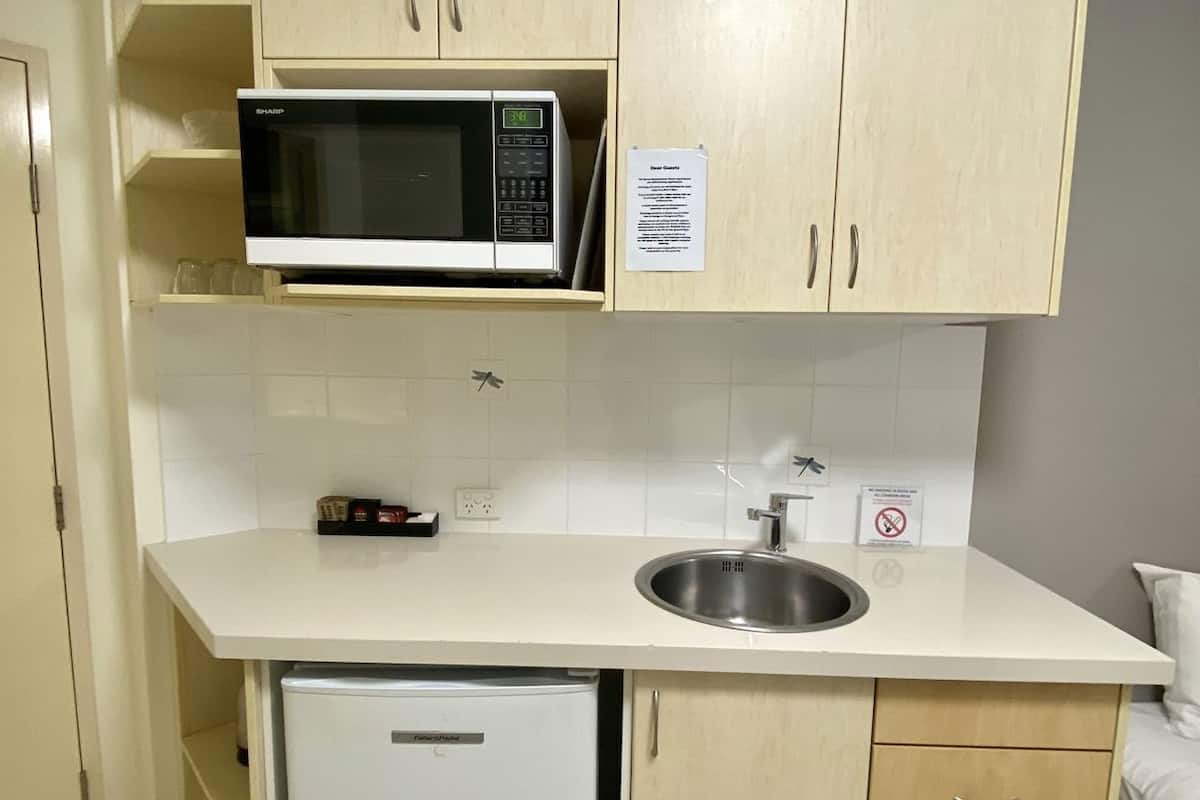 A compact kitchenette with a microwave, a small refrigerator, a sink, and a cabinet with a 'Dear Guests' sign.