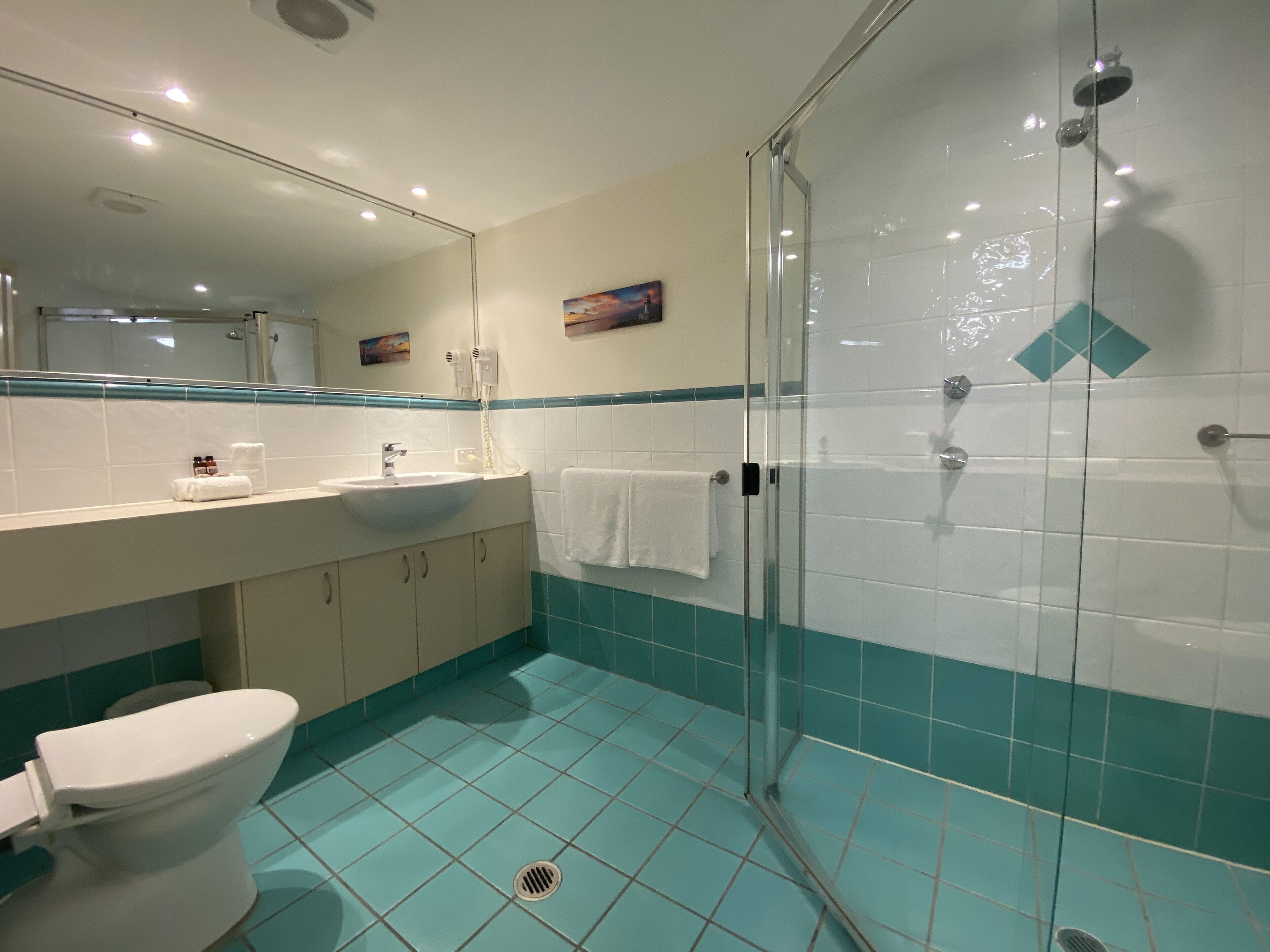 Un baño con ducha de vidrio, lavamanos con espejo y retrete.