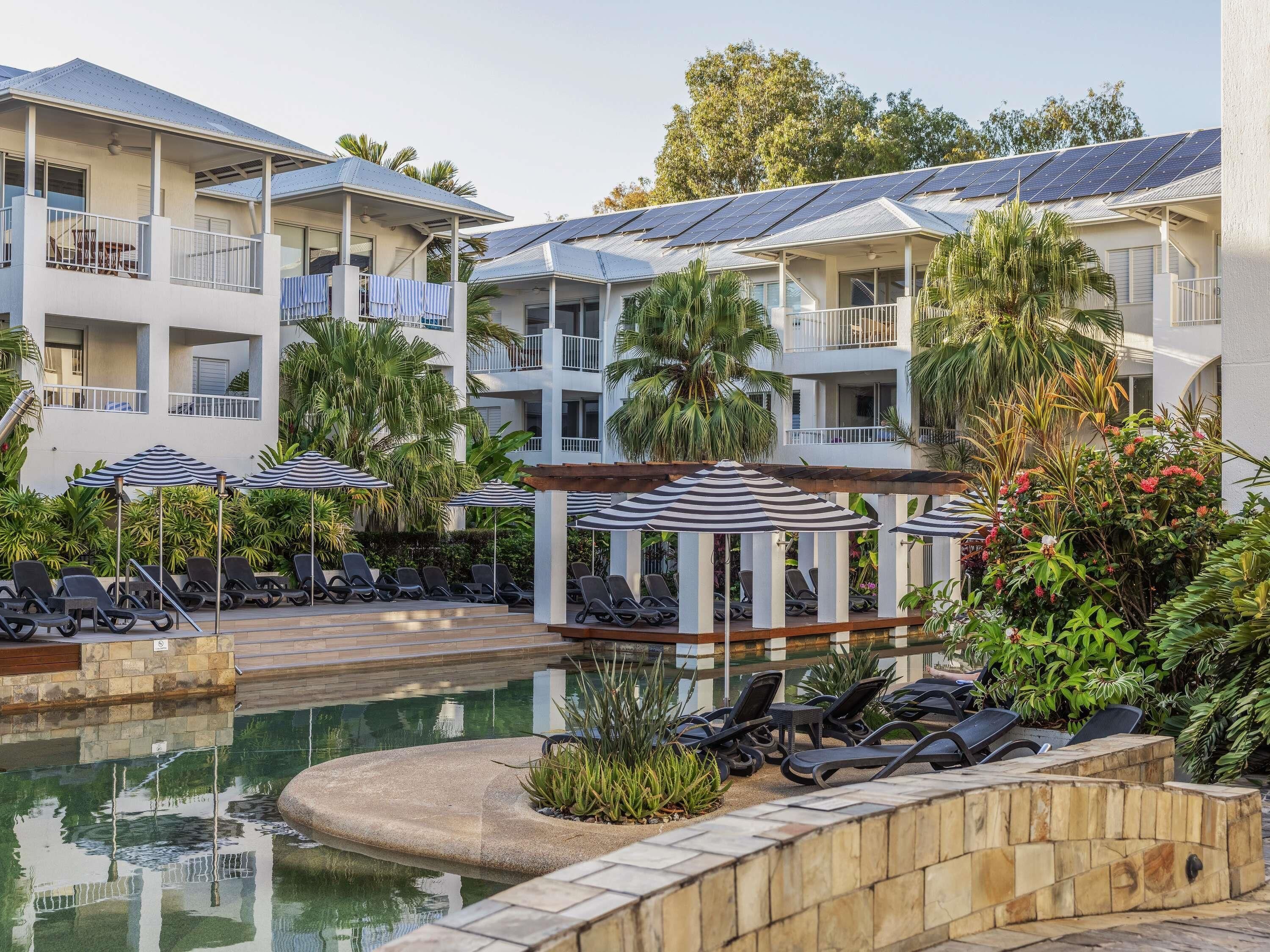 A resort with a swimming pool, sun loungers, umbrellas, and solar panels on the buildings.