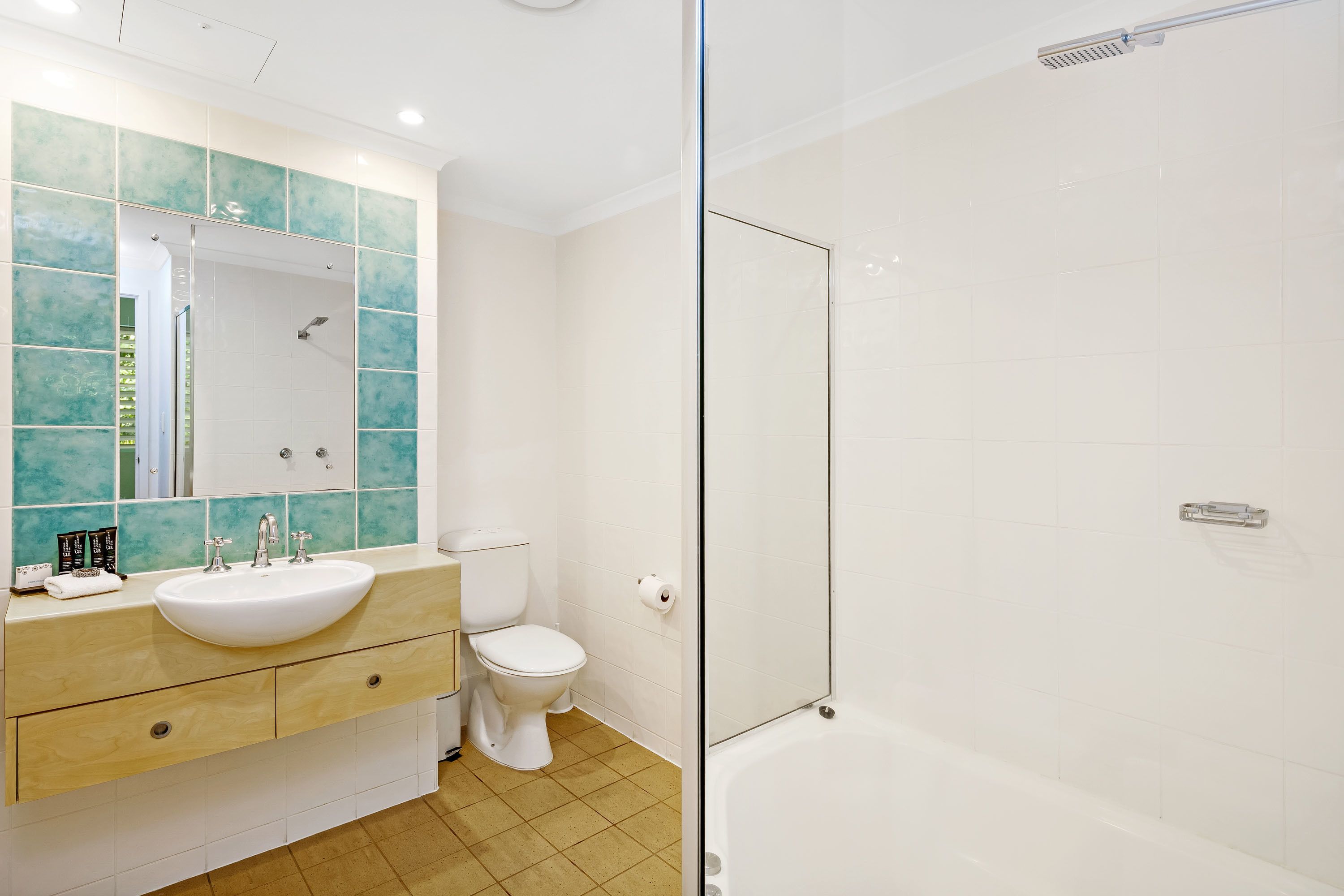 Un baño moderno con lavamanos blanco, inodoro y ducha con mampara de vidrio.