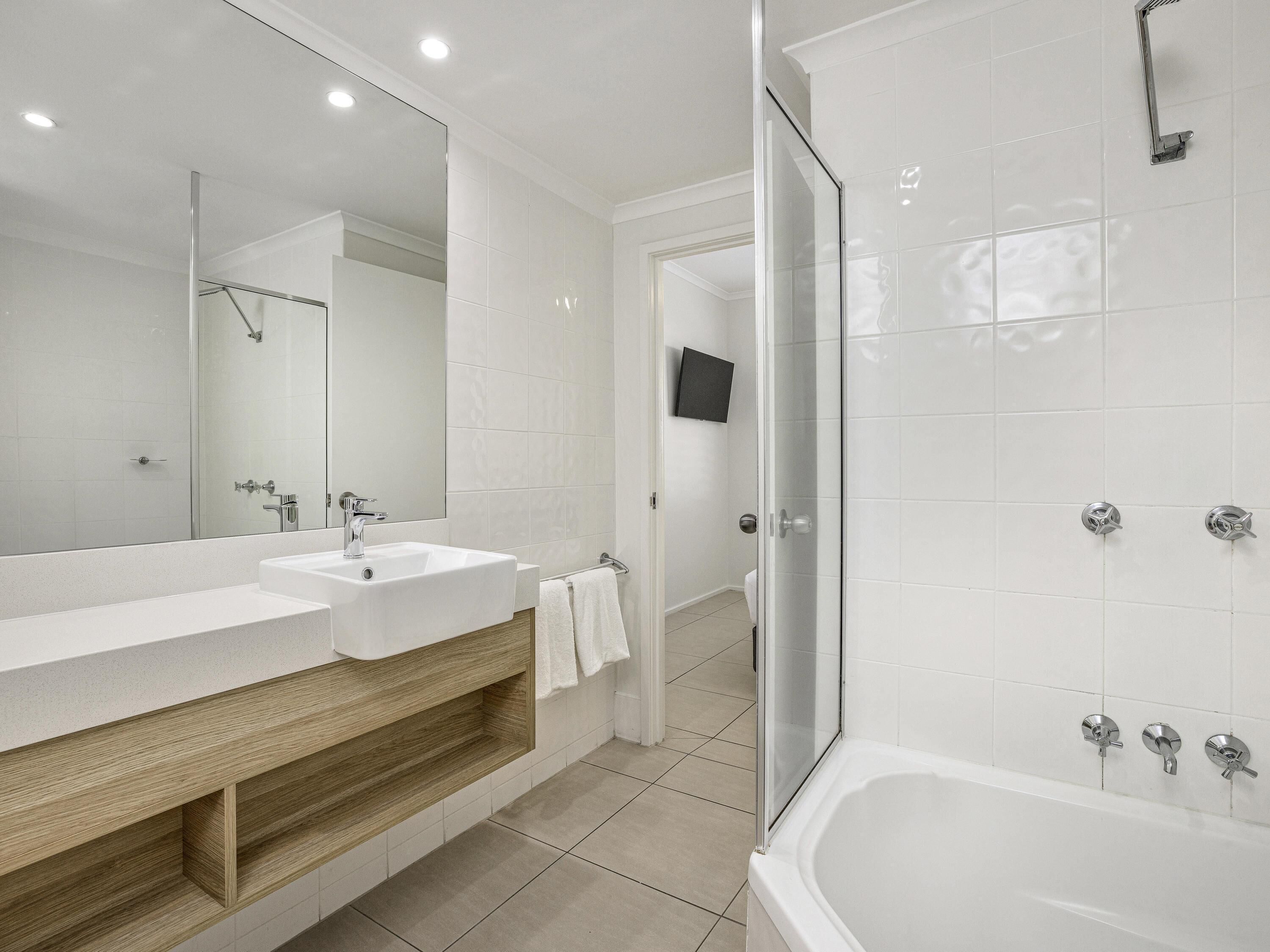 A modern bathroom with a large mirror, two sinks, a shower, and a bathtub.