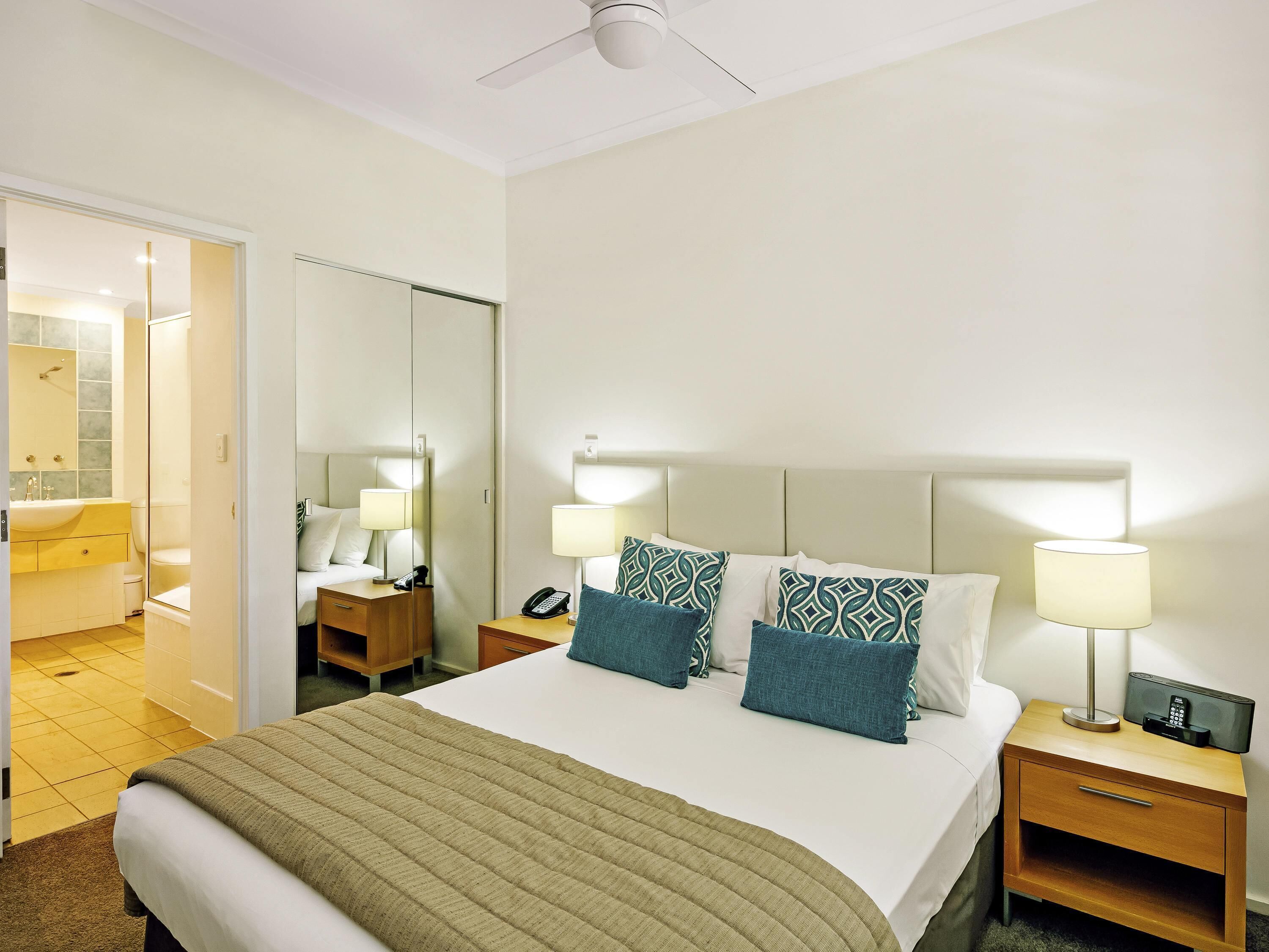 Una habitación de hotel con cama, mesitas de noche, espejo, ducha e inodoro.