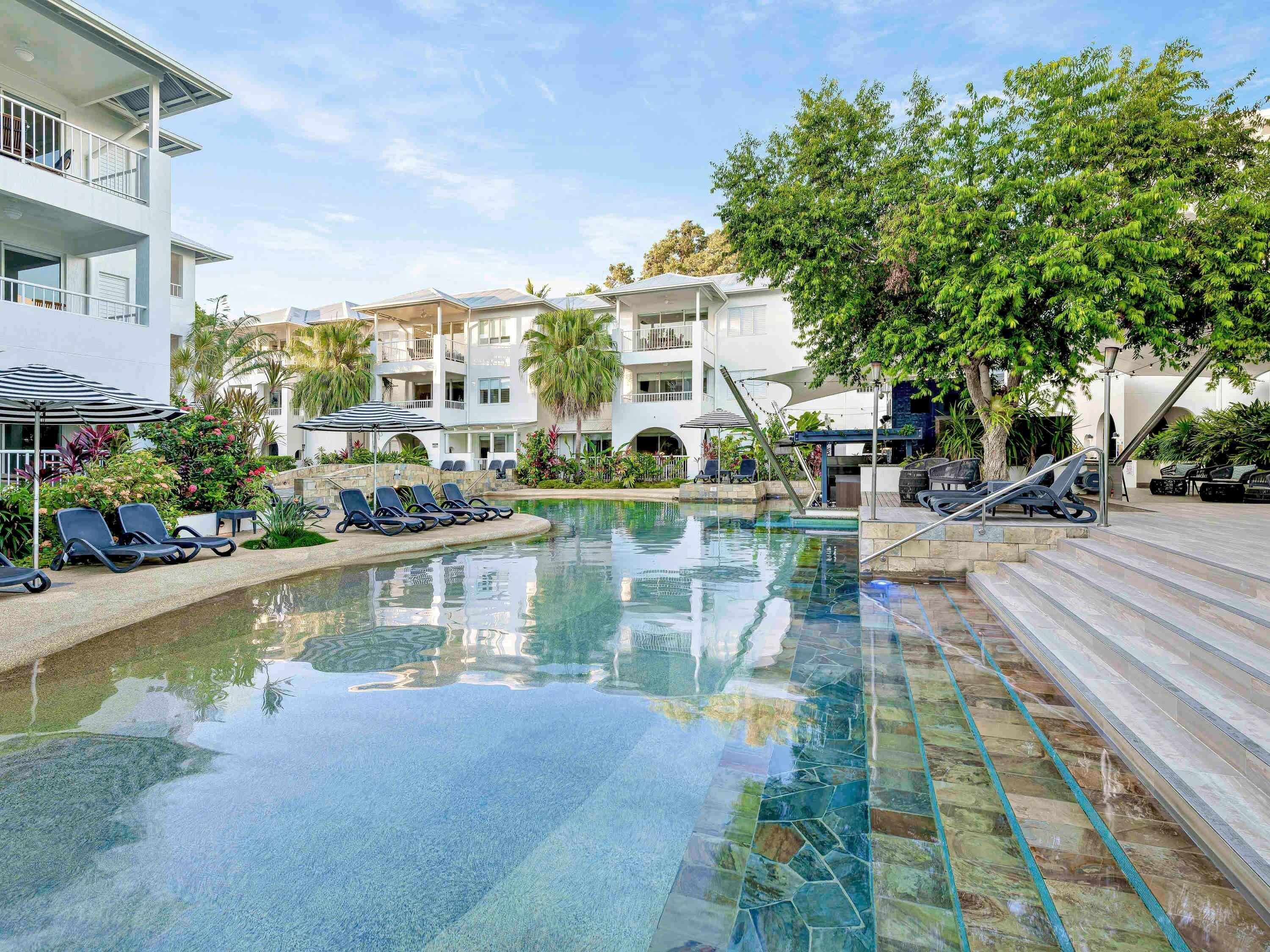 Une piscine avec des chaises longues, un escalier et un immeuble à plusieurs étages doté de balcons.