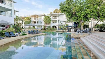 Une piscine avec des chaises longues, un escalier et un immeuble à plusieurs étages doté de balcons.