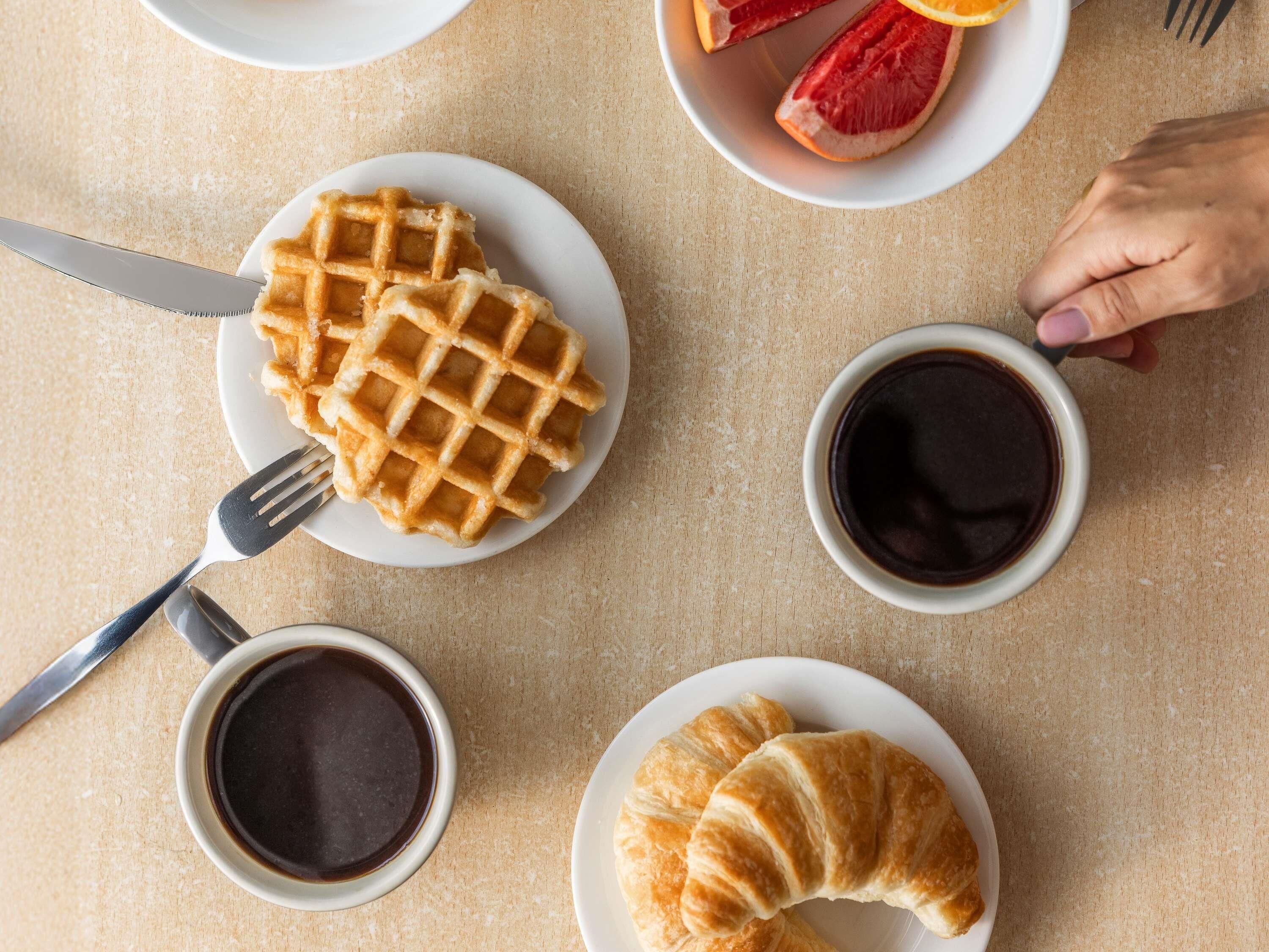 A breakfast setting with waffles, croissants, orange slices, and coffee on a table.