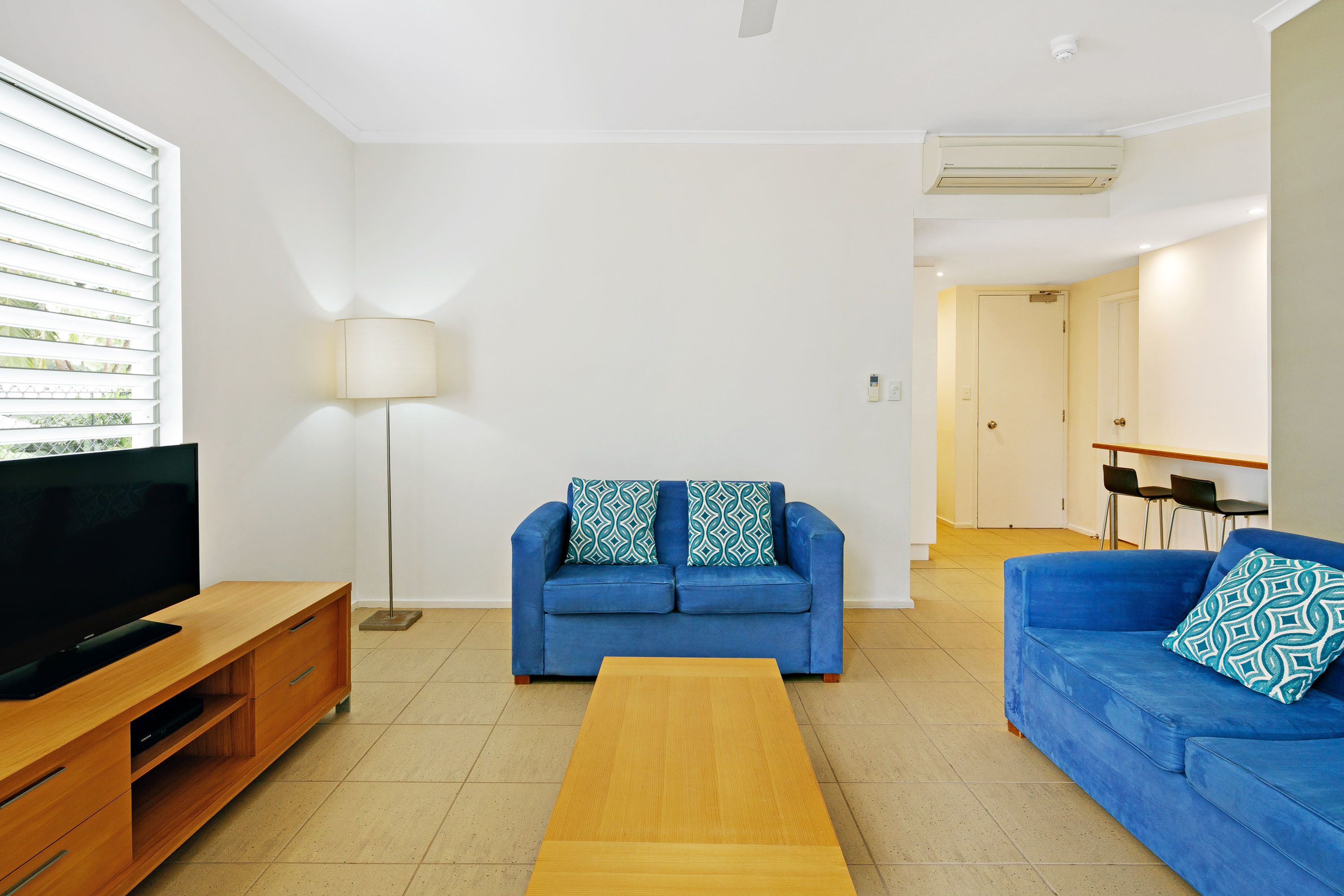 A modern living room with a blue sofa, a wooden coffee table, a TV on a wooden stand, and a floor lamp.