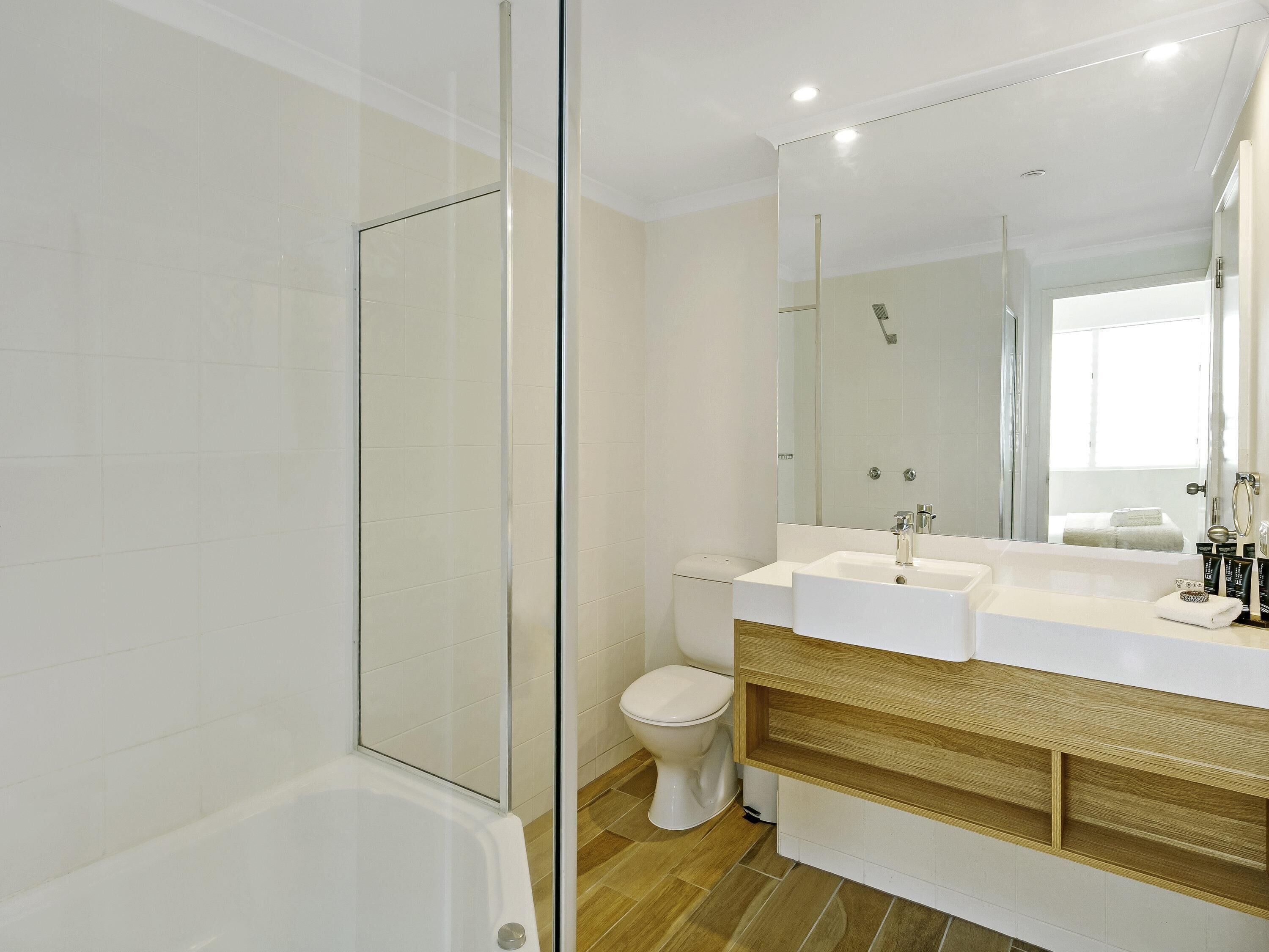 A modern bathroom with a glass shower enclosure, a white bathtub, a toilet, and a vanity with a mirror.
