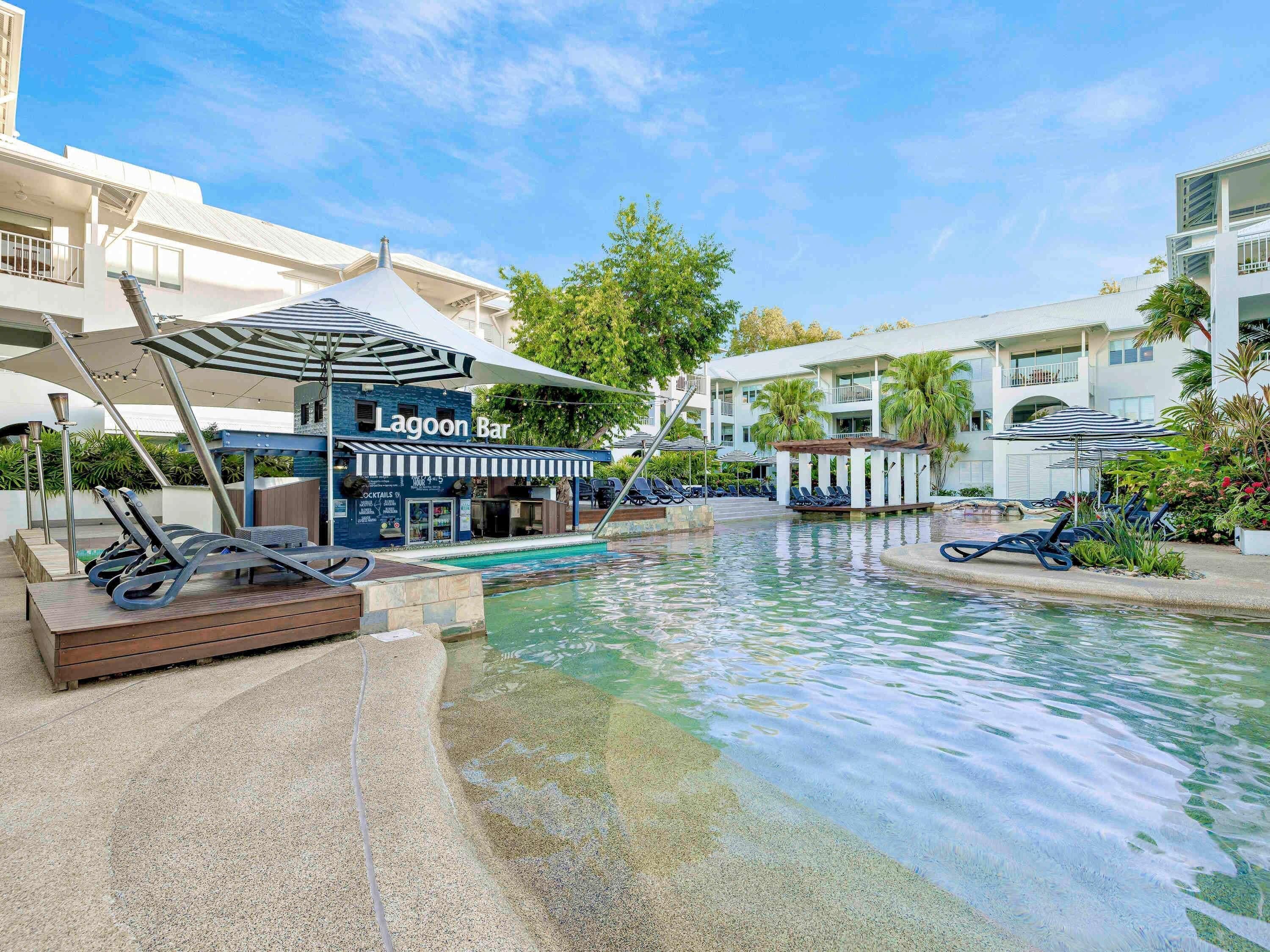 Un espace piscine avec des chaises longues, un bar appelé « Lagoon Bar », et un bâtiment doté de balcons.