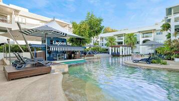 A pool area with lounge chairs, a bar named 'Lagoon Bar,' and a building with balconies.