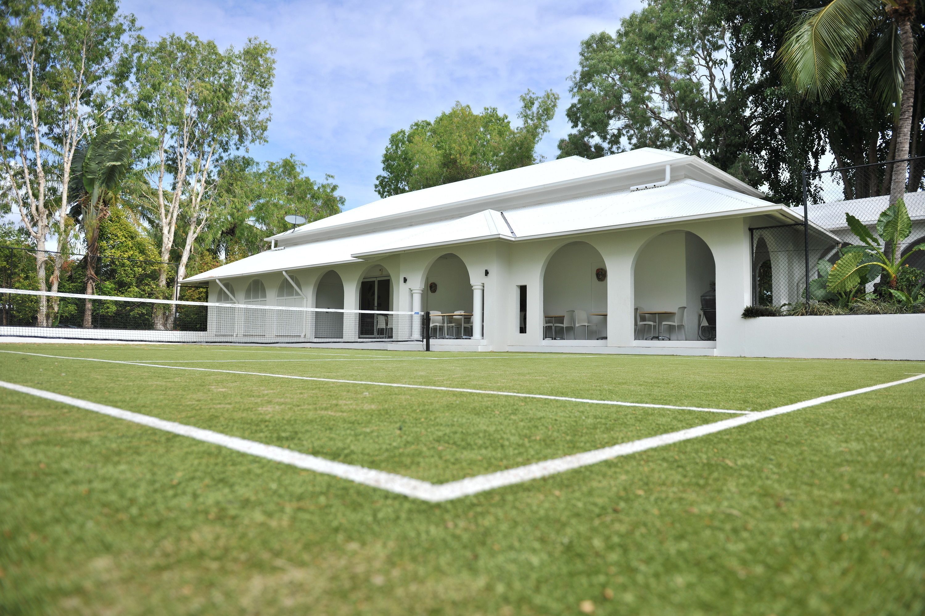 A white building with multiple arches and a tennis court in front.