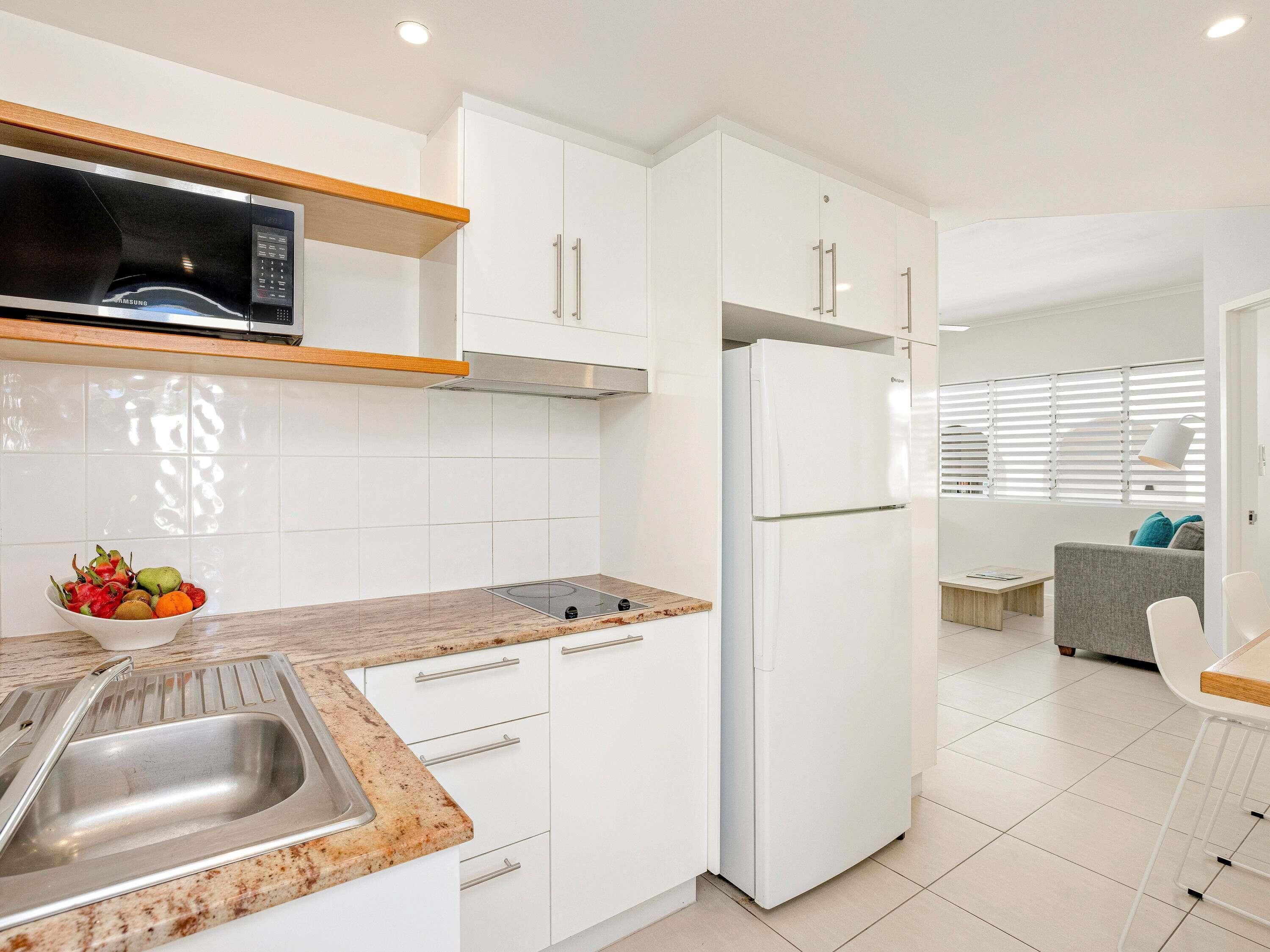 A modern kitchen with white cabinets, a built-in microwave, a stainless steel sink, and a refrigerator.