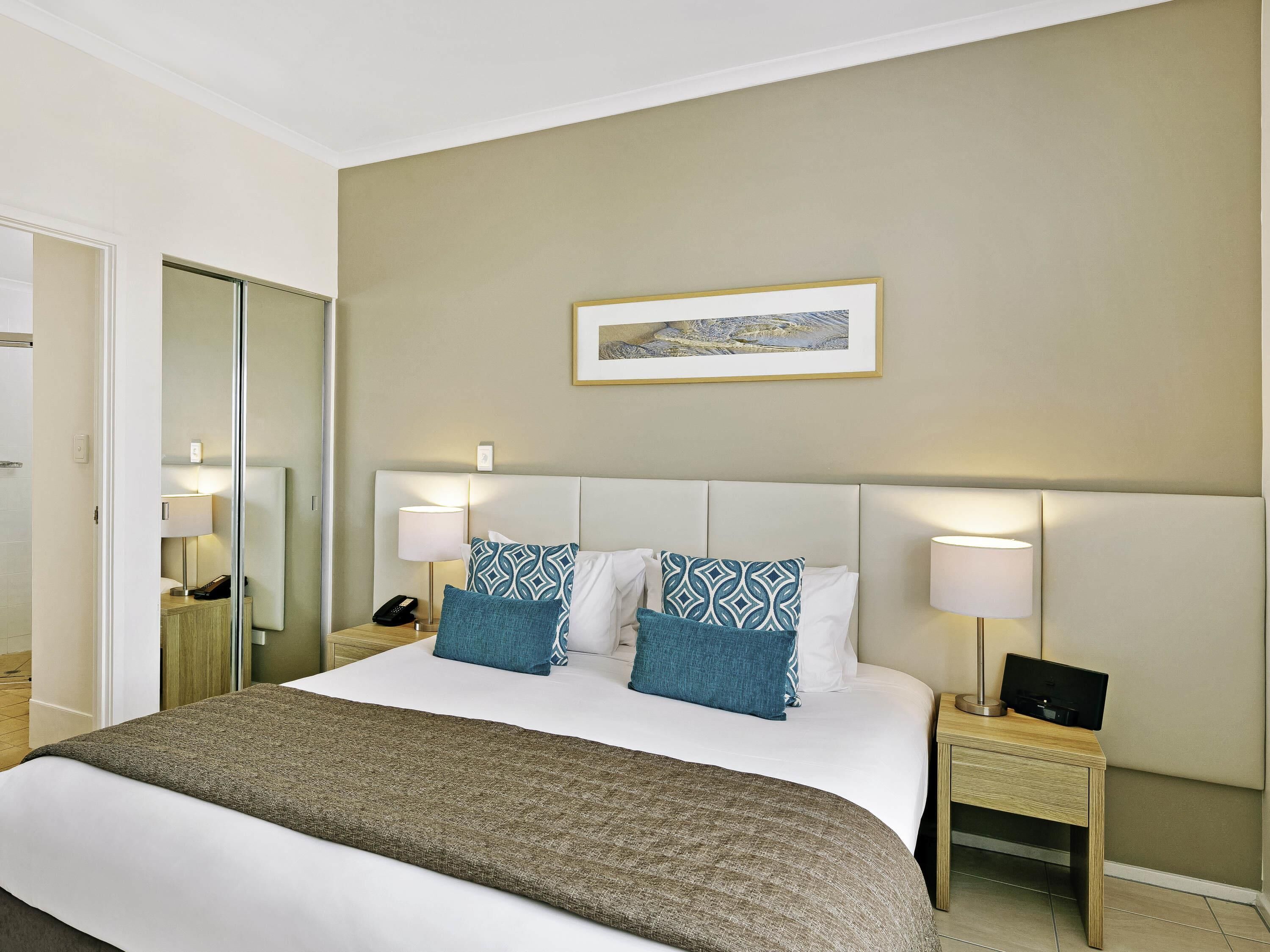 A hotel room with a large bed, two bedside tables with lamps, a mirror, and a framed picture on the wall.