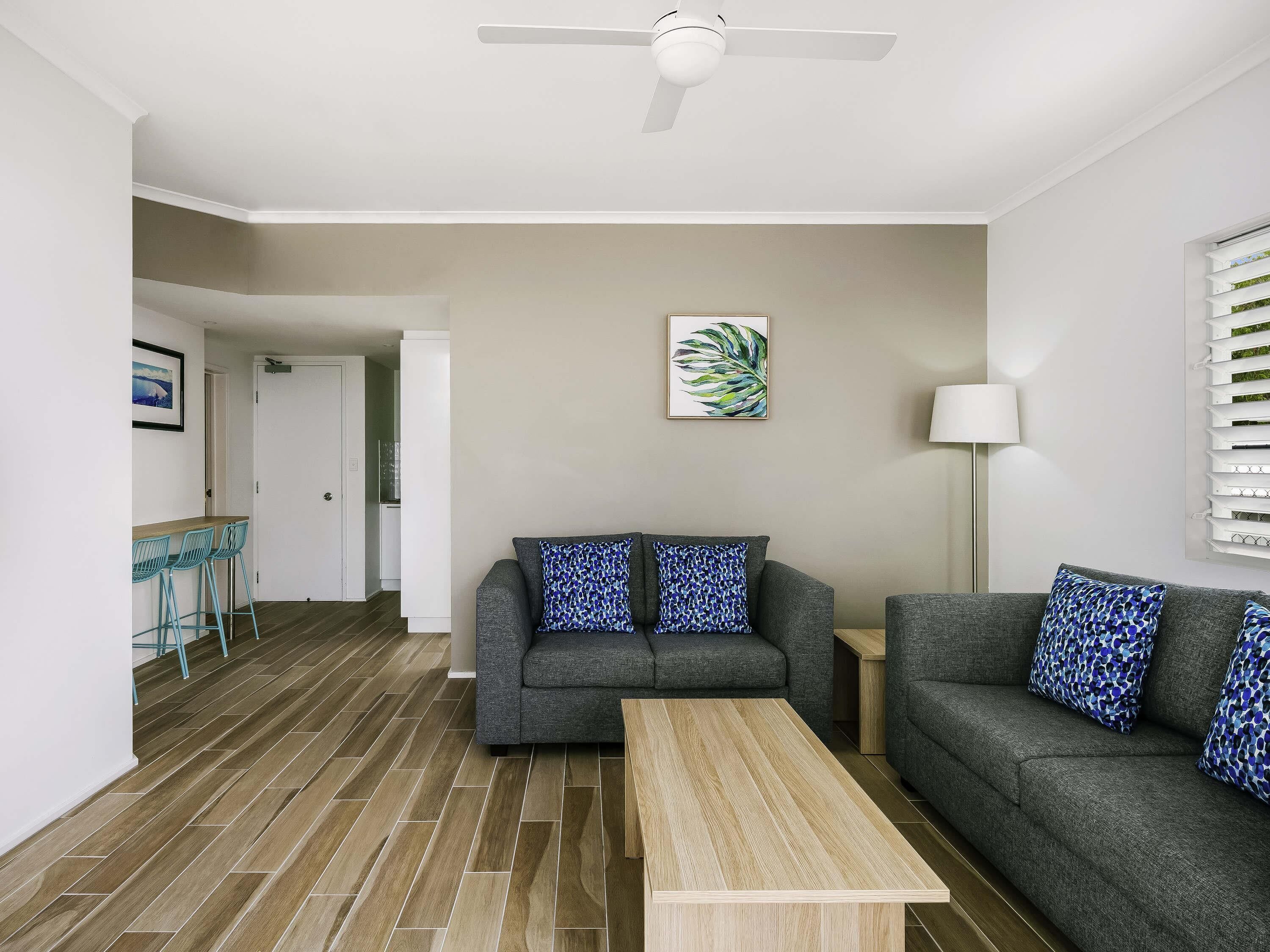 A modern living room with a grey sofa, a wooden coffee table, and a ceiling fan.