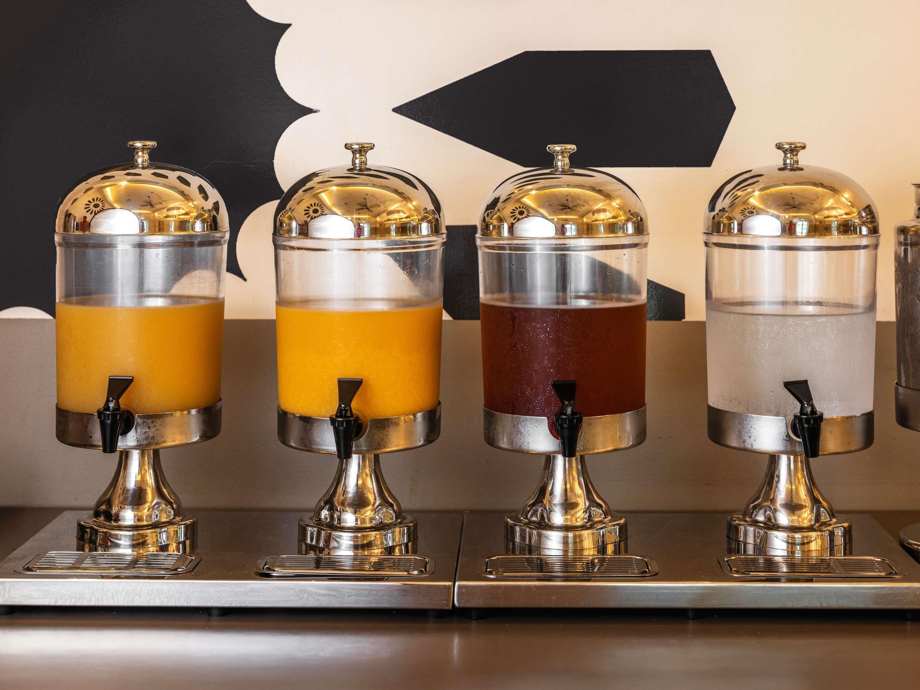 Cuatro dispensadores de bebidas con contenedores transparentes y tapas metálicas.