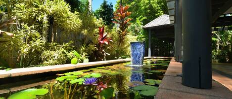 Un jardín tranquilo con un estanque, abundante vegetación y una estructura arquitectónica tradicional.