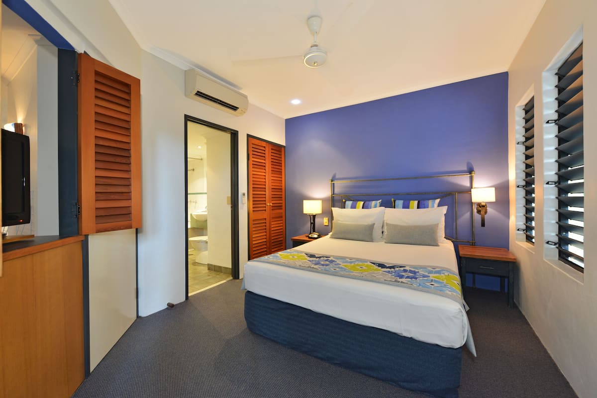Une chambre d’hôtel équipée d’un lit, d’un bureau, d’une armoire et d’une fenêtre avec des stores.