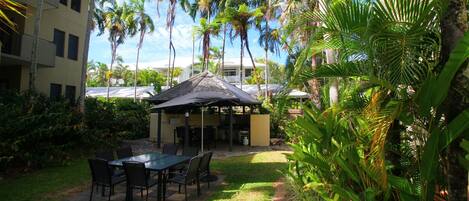 A patio area with a table and chairs, surrounded by lush greenery and palm trees.