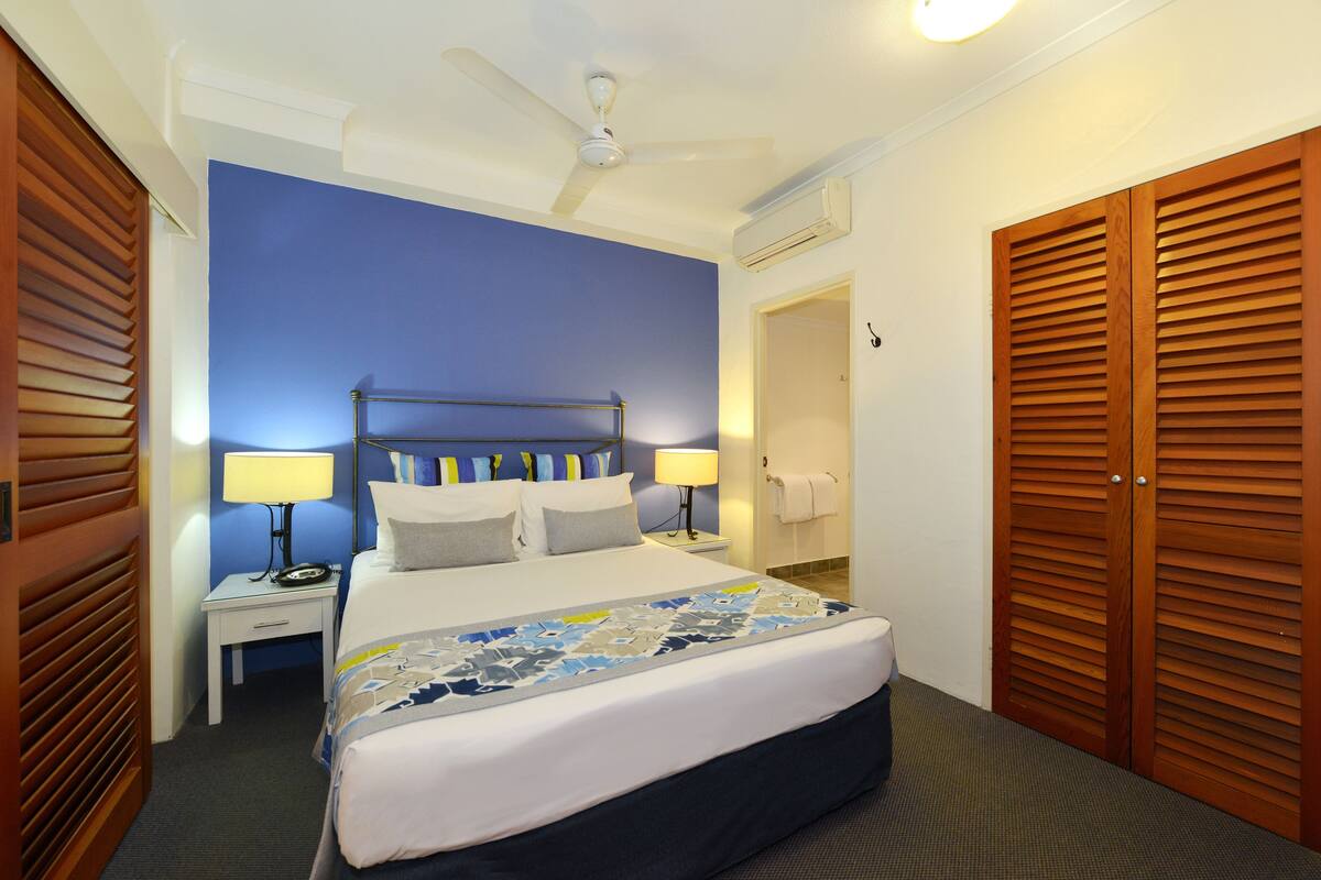 Une chambre d’hôtel avec un lit, des tables de chevet, un ventilateur de plafond et des armoires en bois.