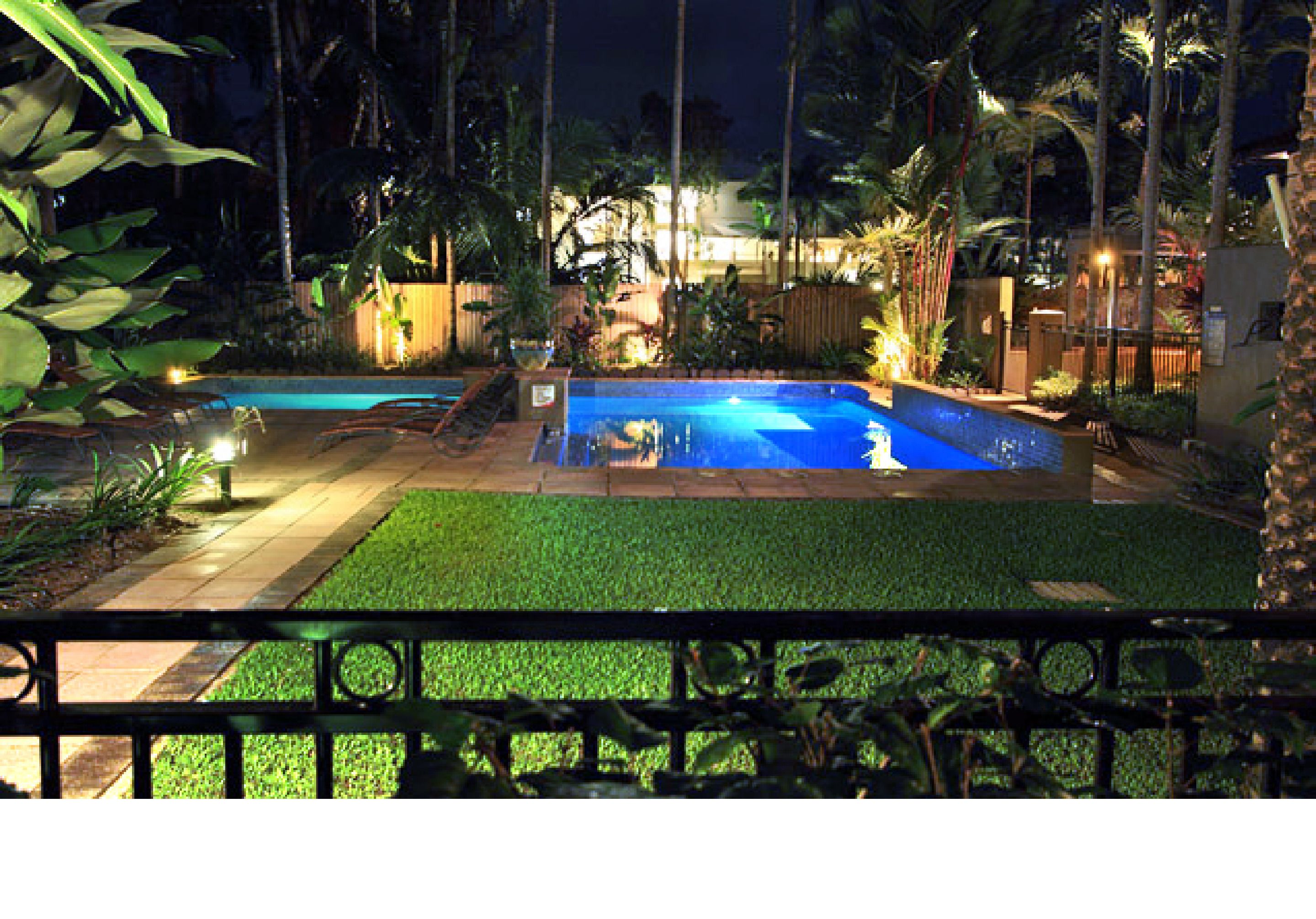 A swimming pool surrounded by palm trees and a well-lit patio area.
