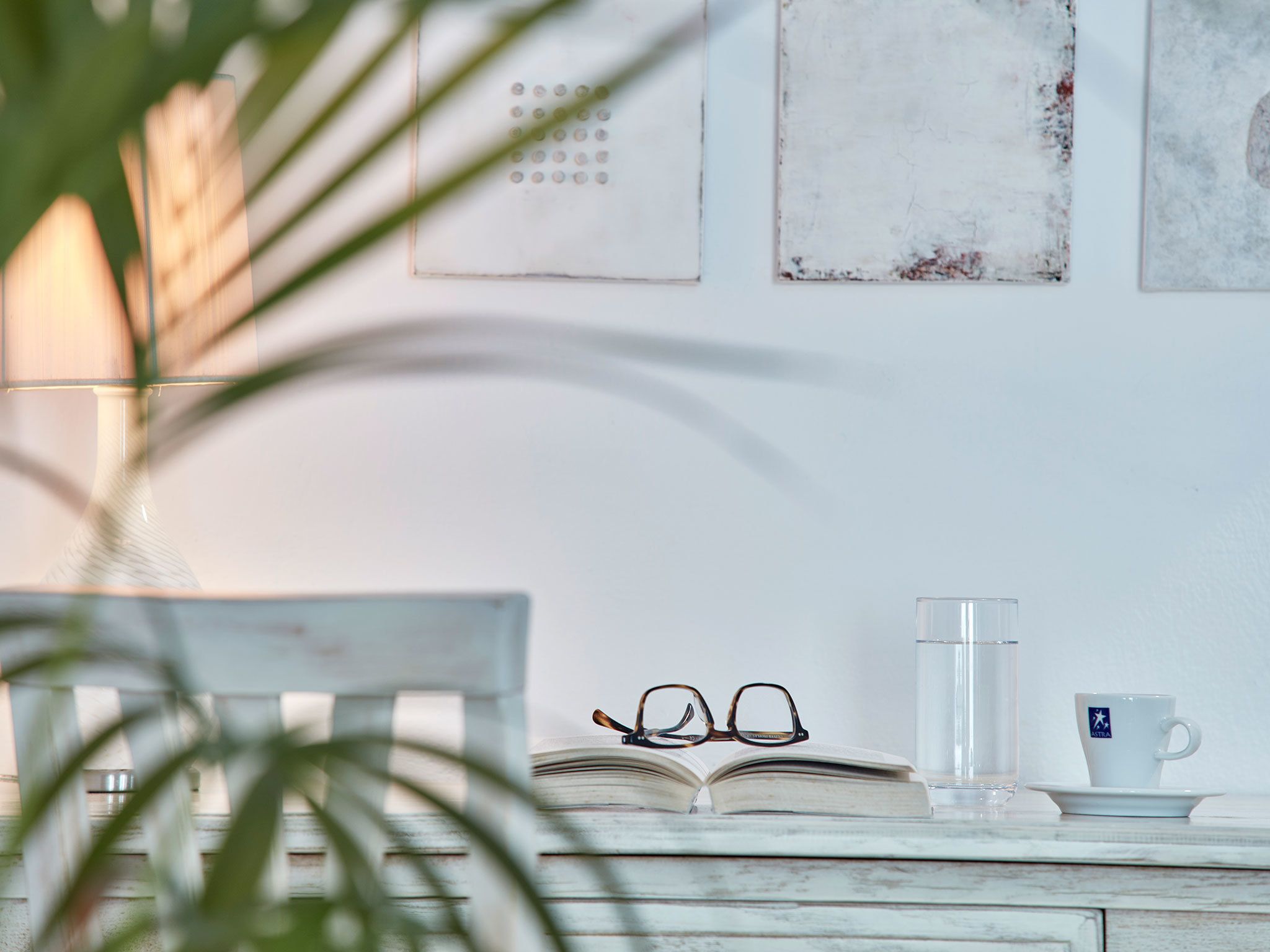 A wooden table with a book, glasses, a glass of water, and a cup on a white surface.