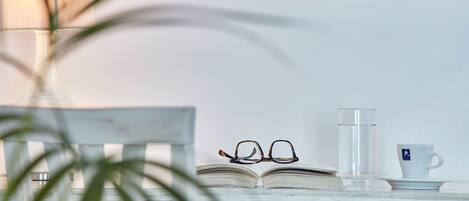 A wooden table with a book, glasses, a glass of water, and a cup on a white surface.