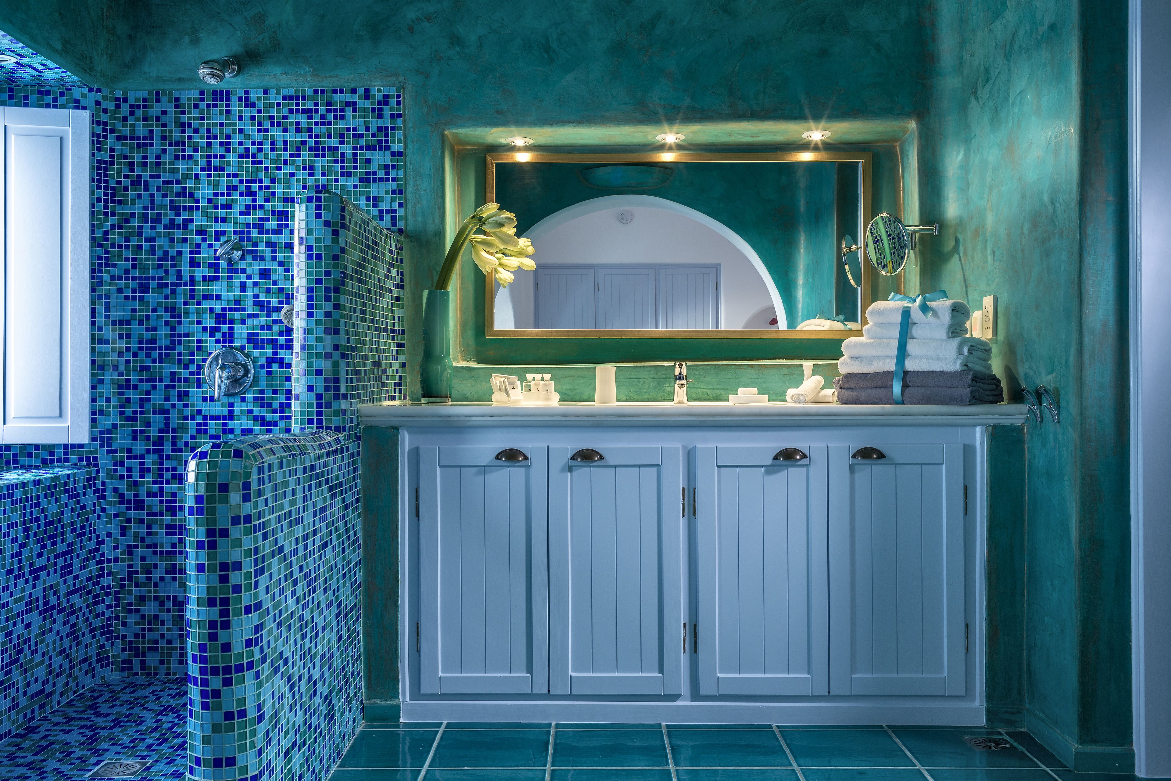 Un baño con suelo de baldosas, un lavabo con espejo y un perchero con toallas.