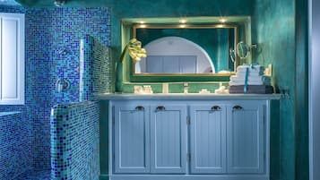 Un baño con suelo de baldosas, un lavabo con espejo y un perchero con toallas.