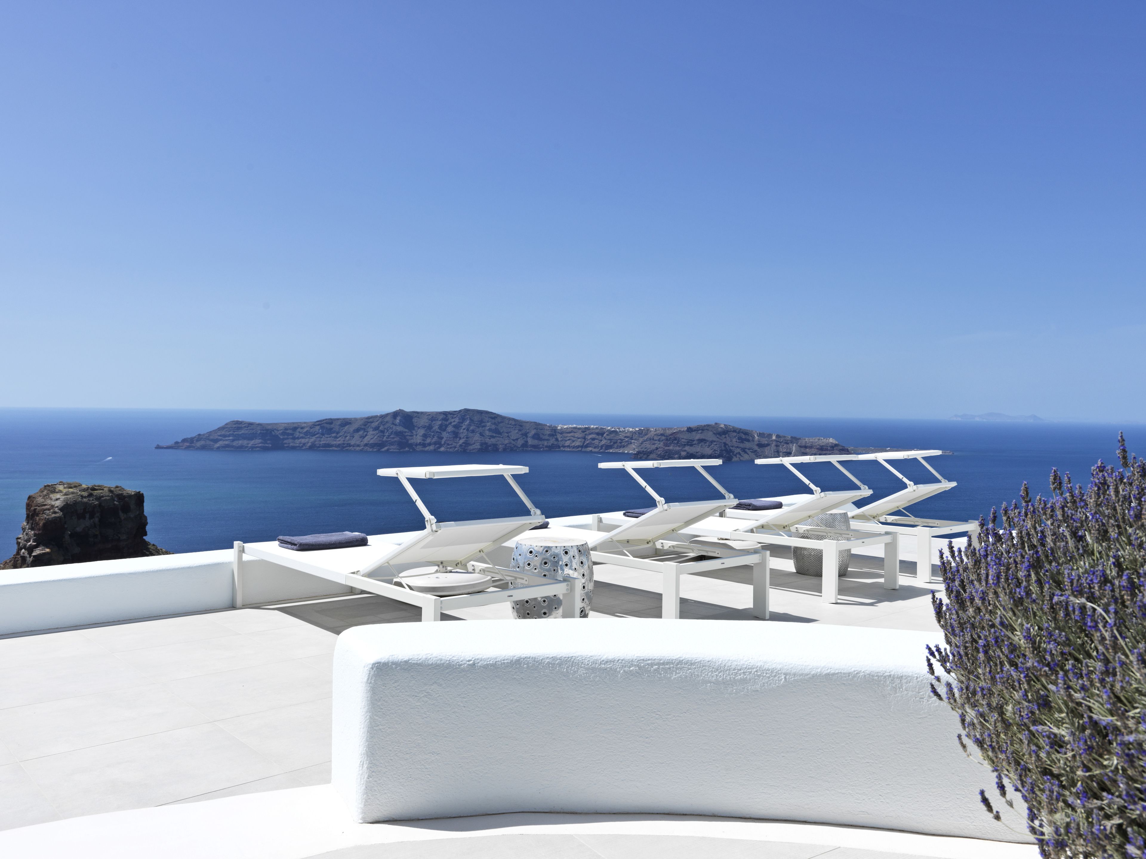 Une terrasse dotée de chaises longues blanches et offrant une vue sur la mer et une île lointaine.
