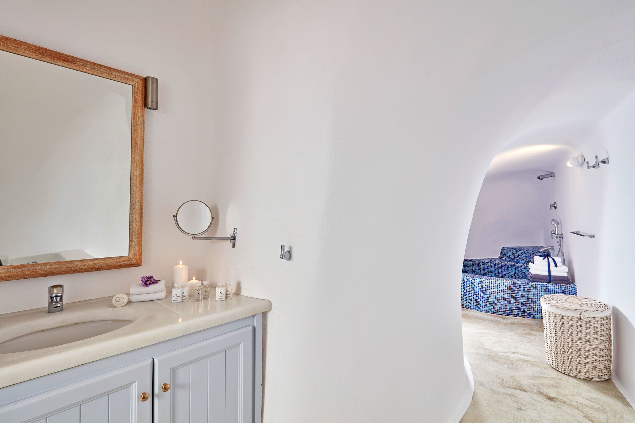 Un bagno con lavandino, specchio e articoli da toilette. Sullo sfondo, un'area doccia con piastrelle blu.