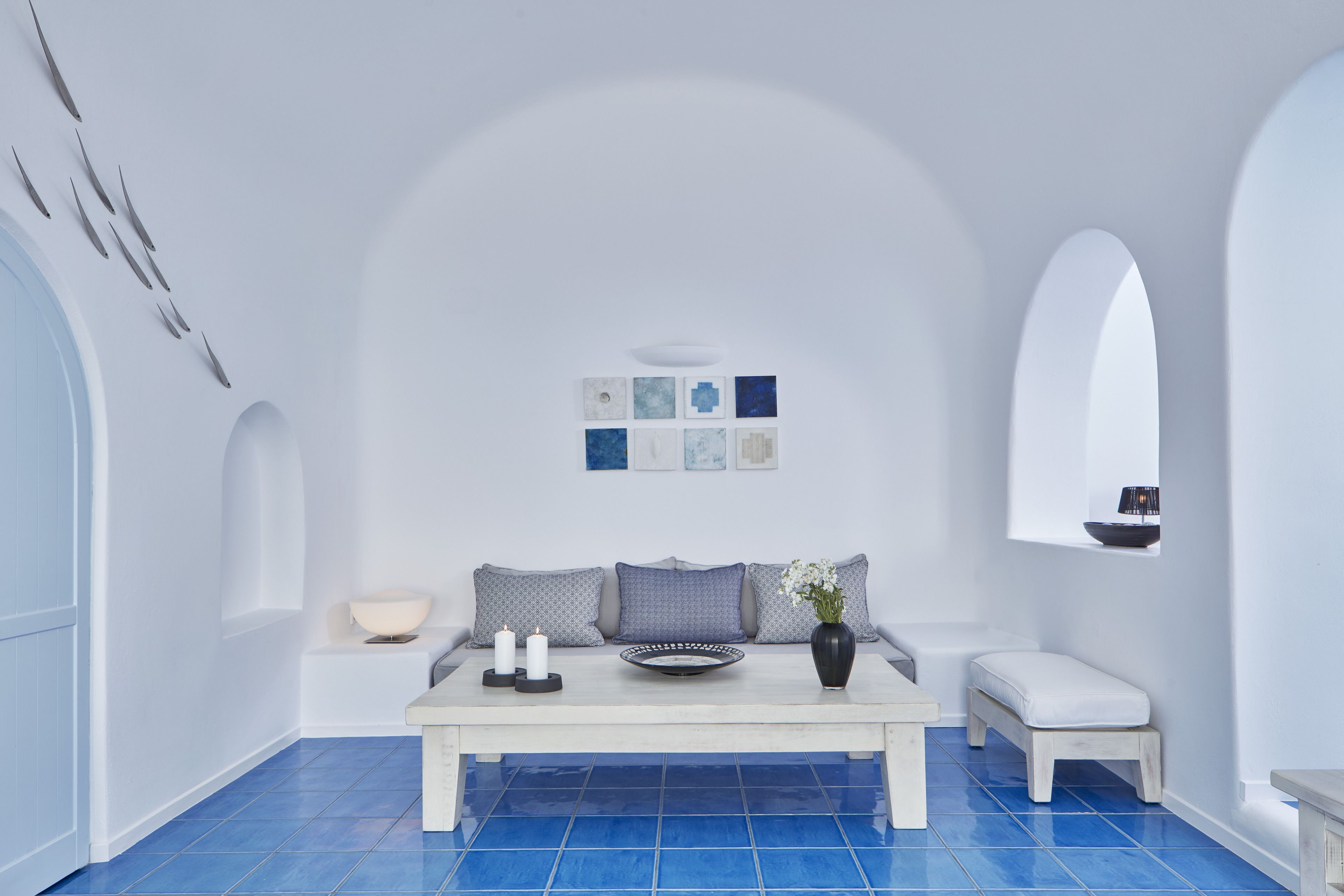 A modern, minimalist room with a white sofa, a small table with candles, and a blue-tiled floor.