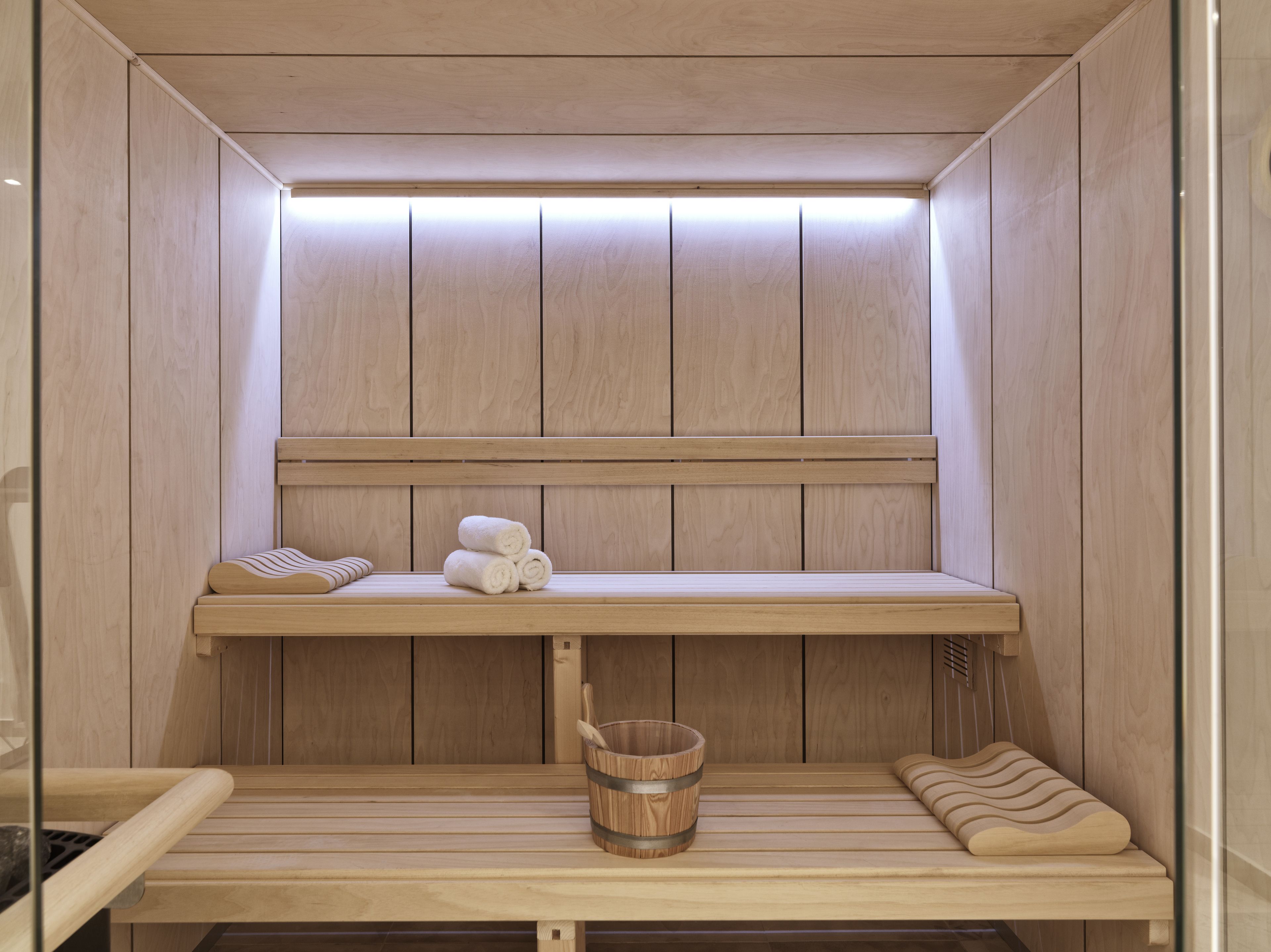 A wooden sauna with a bench, a shelf with towels, and a bucket.