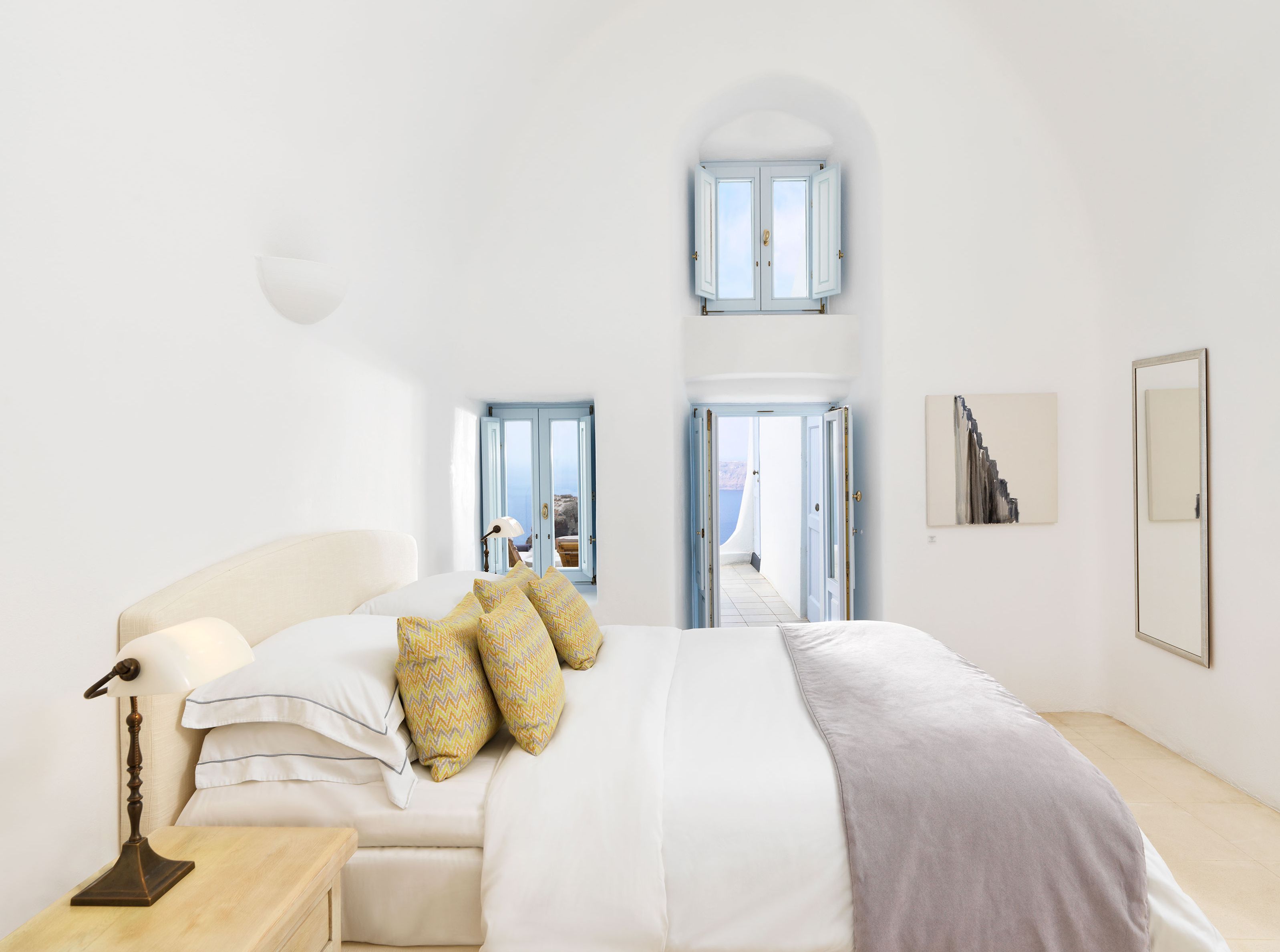 Une chambre spacieuse avec un grand lit, une table de chevet et une lampe de bureau. Deux portes donnent sur un balcon avec vue sur la mer.