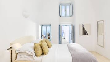 Une chambre spacieuse avec un grand lit, une table de chevet et une lampe de bureau. Deux portes donnent sur un balcon avec vue sur la mer.