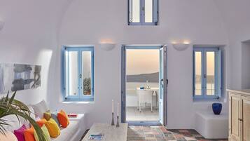 Una habitación con un sofá blanco, almohadones coloridos, una mesa con una revista y vistas a un balcón con mesa y sillas.