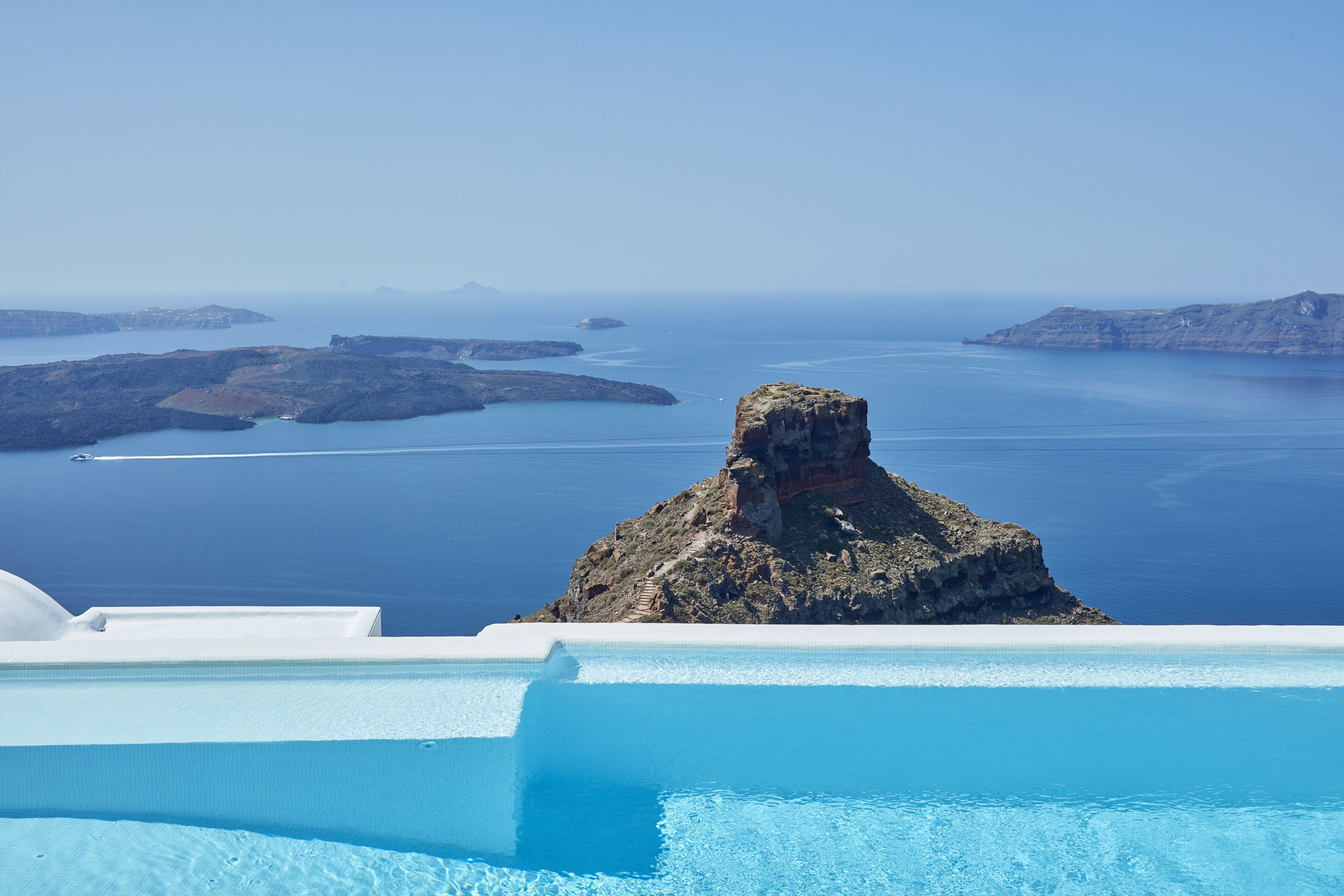 Una vista despejada de una piscina con un afloramiento rocoso en primer plano, rodeada de aguas azules y tranquilas y de islas a lo lejos.