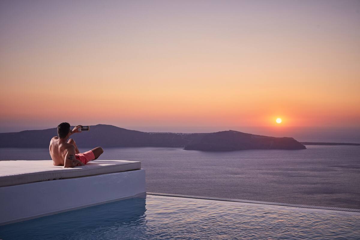 A man taking a photo by a pool with a sunset view.