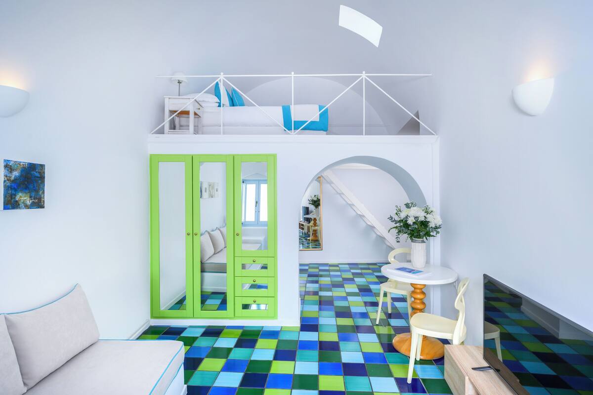 A room with a bunk bed, a green wardrobe, a round table with chairs, and a colorful checkered floor.
