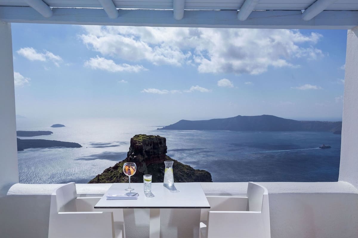 A table with a view of the sea and islands, two glasses of drink, and a bottle of water.
