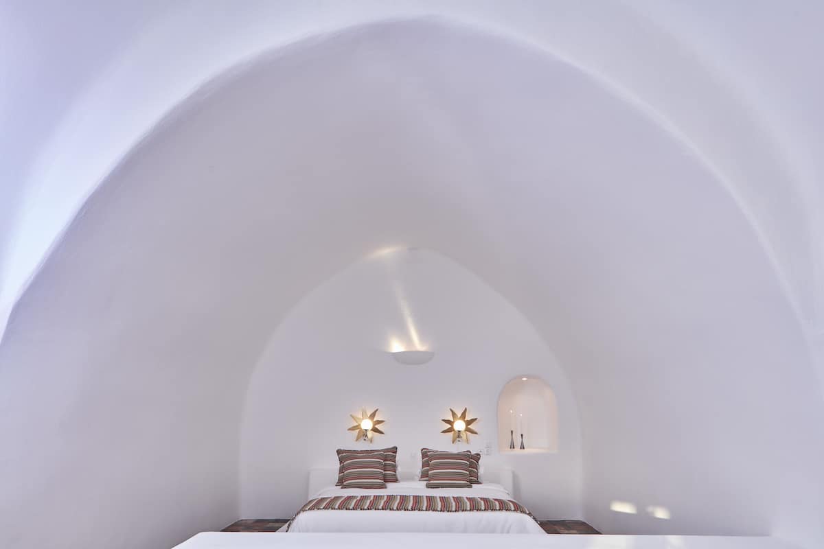 A bedroom with a vaulted ceiling, a bed with striped bedding, and two wall-mounted star-shaped light fixtures.