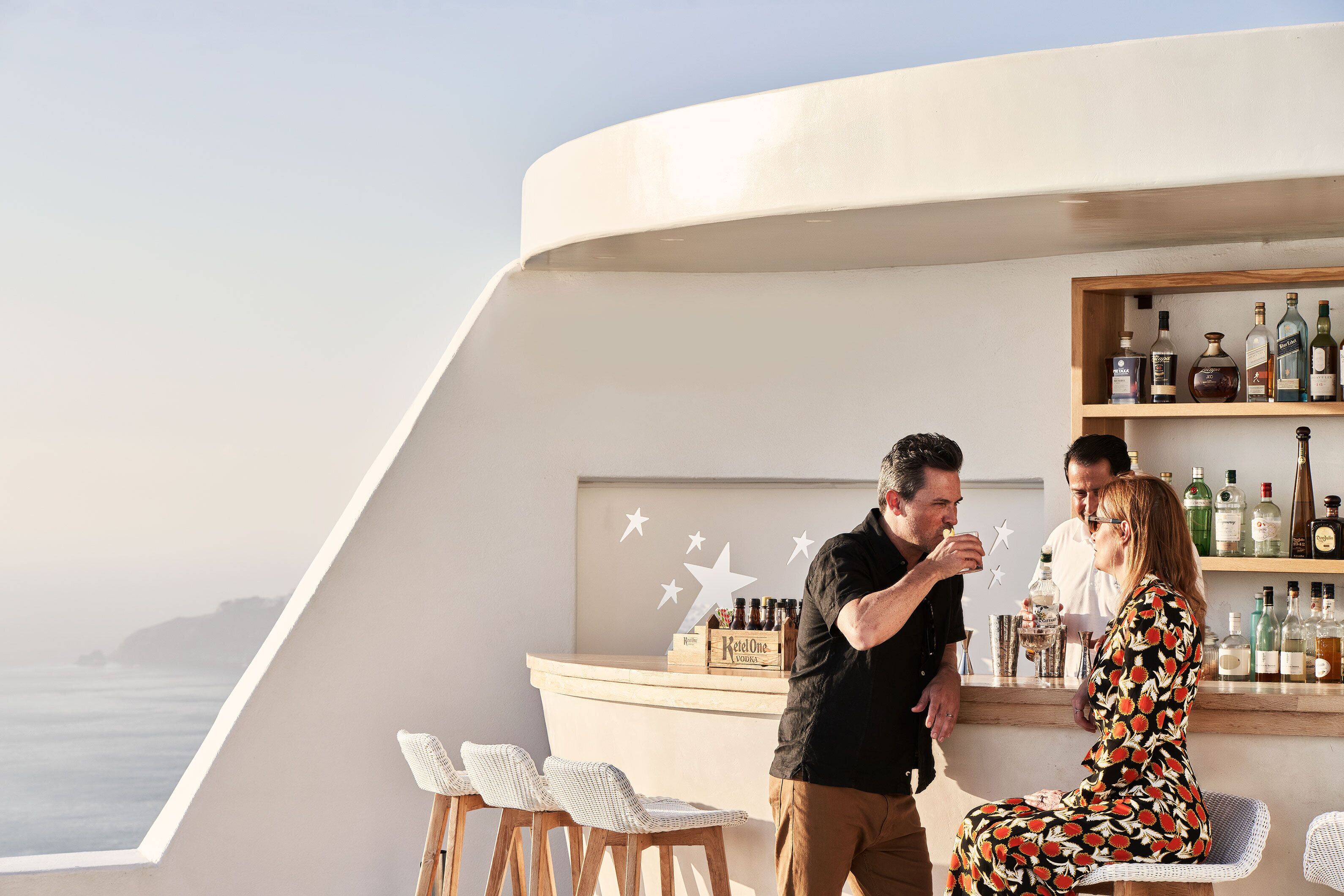 A bar area with a curved counter, wicker chairs, and a view of the sea.
