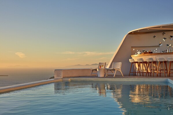 A poolside area with lounge chairs and a bar, overlooking the sea. - Astra Suites (Santorini)