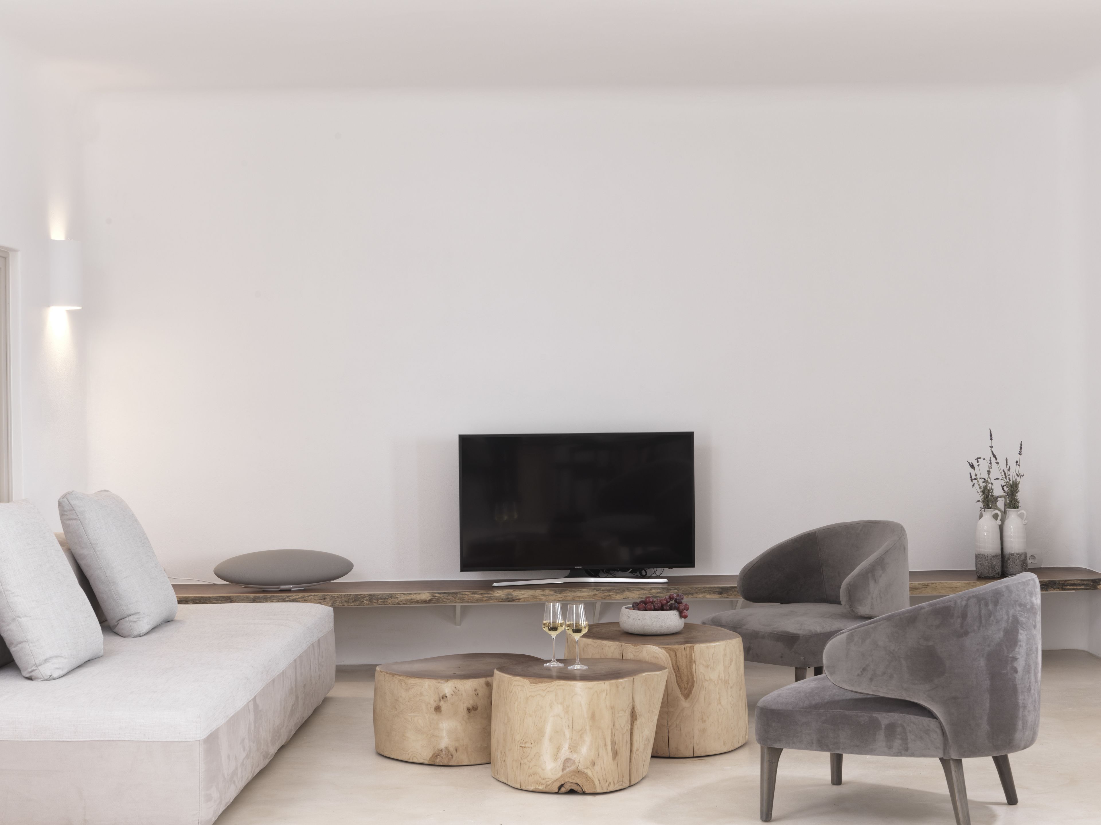 A modern living room with a flat-screen TV, grey upholstered furniture, and wooden side tables.